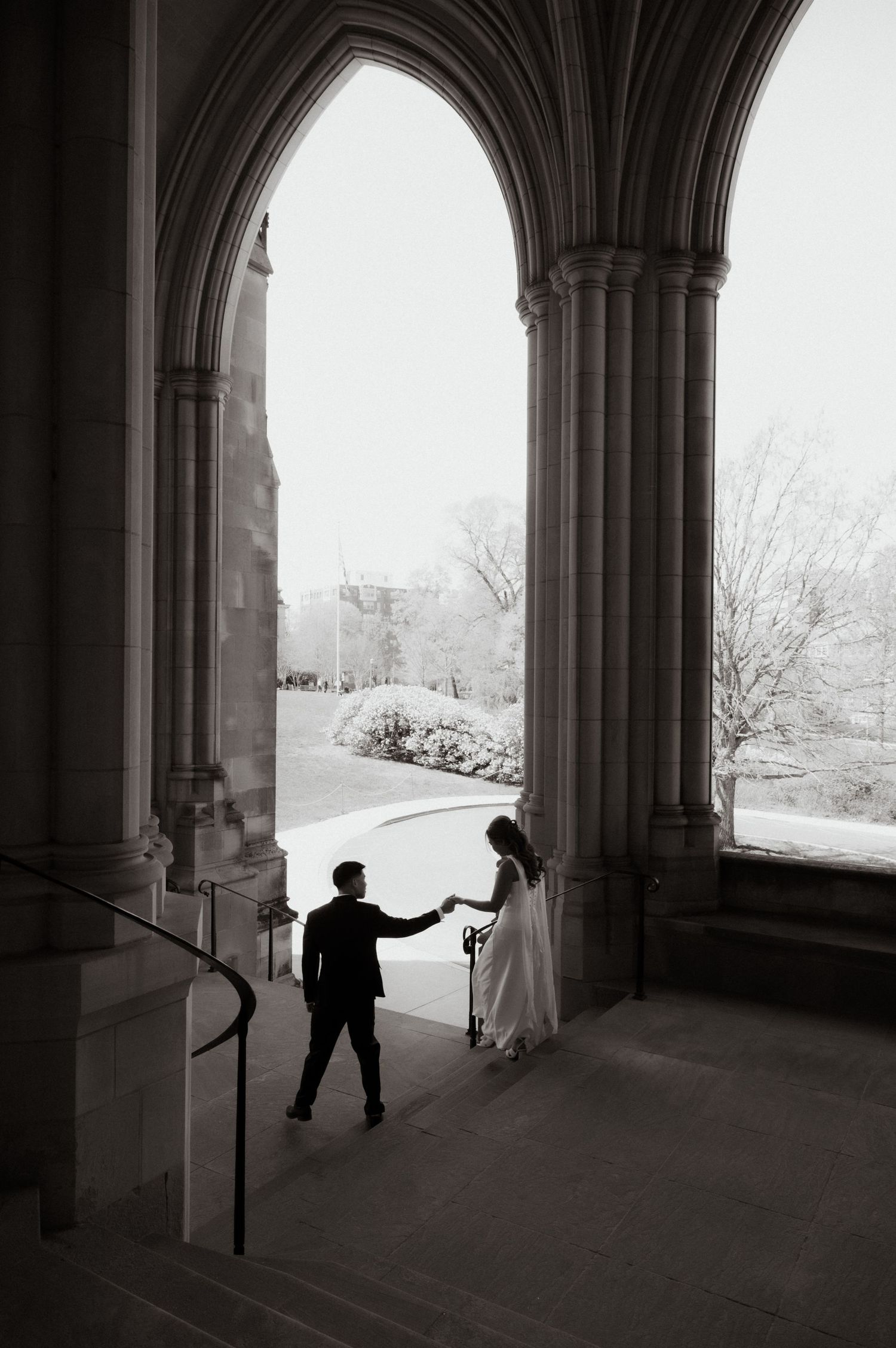 Black and white photo of bride and groom holding hands under cathedral arches in winter.