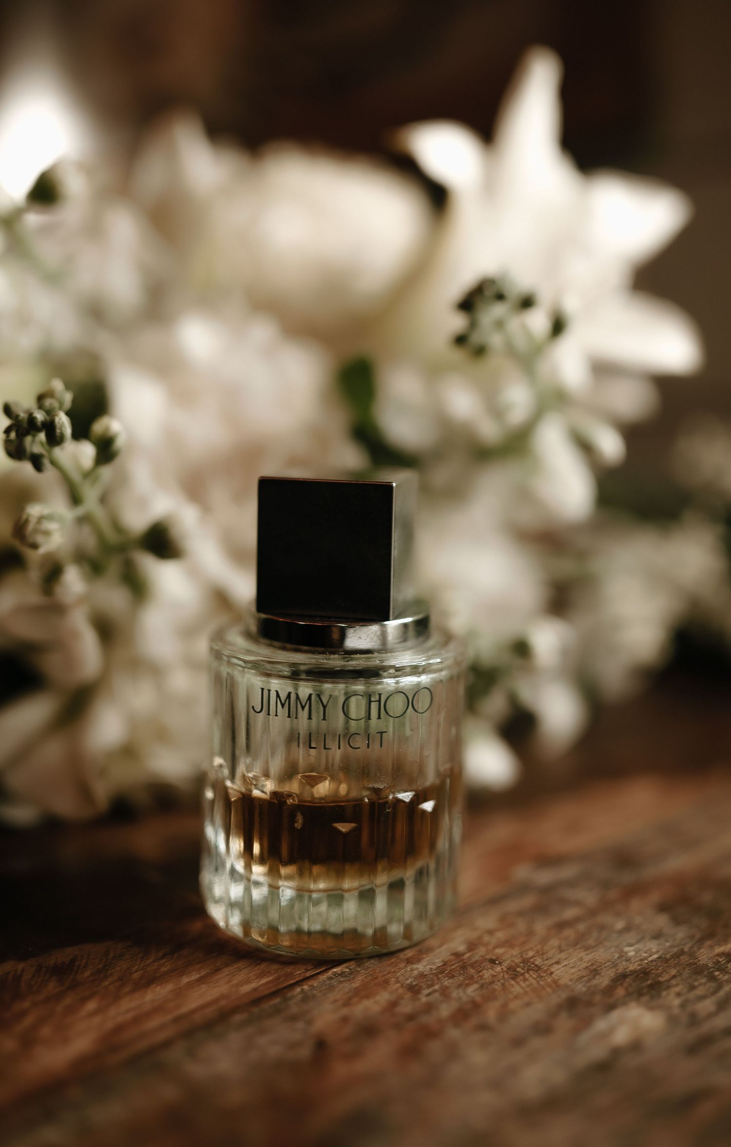 Jimmy Choo perfume bottle displayed on rustic wooden surface with white flowers in soft focus background.