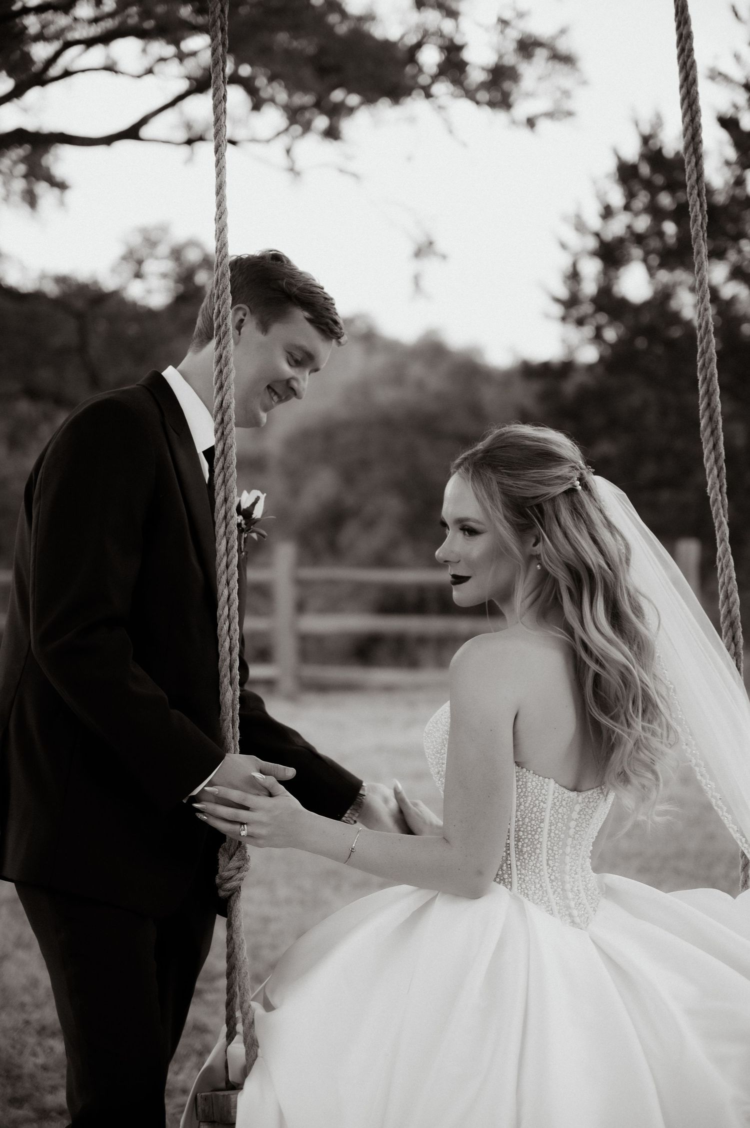 A romantic moment between newlyweds on a swing set captured in black and white photography.