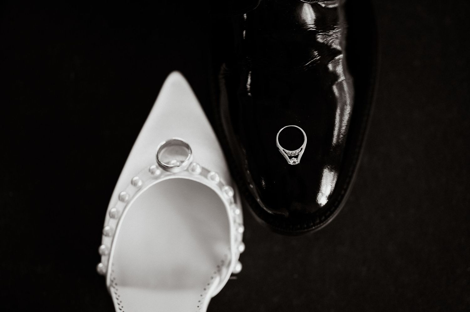 Wedding rings photographed in dramatic black and white lighting on a reflective surface.