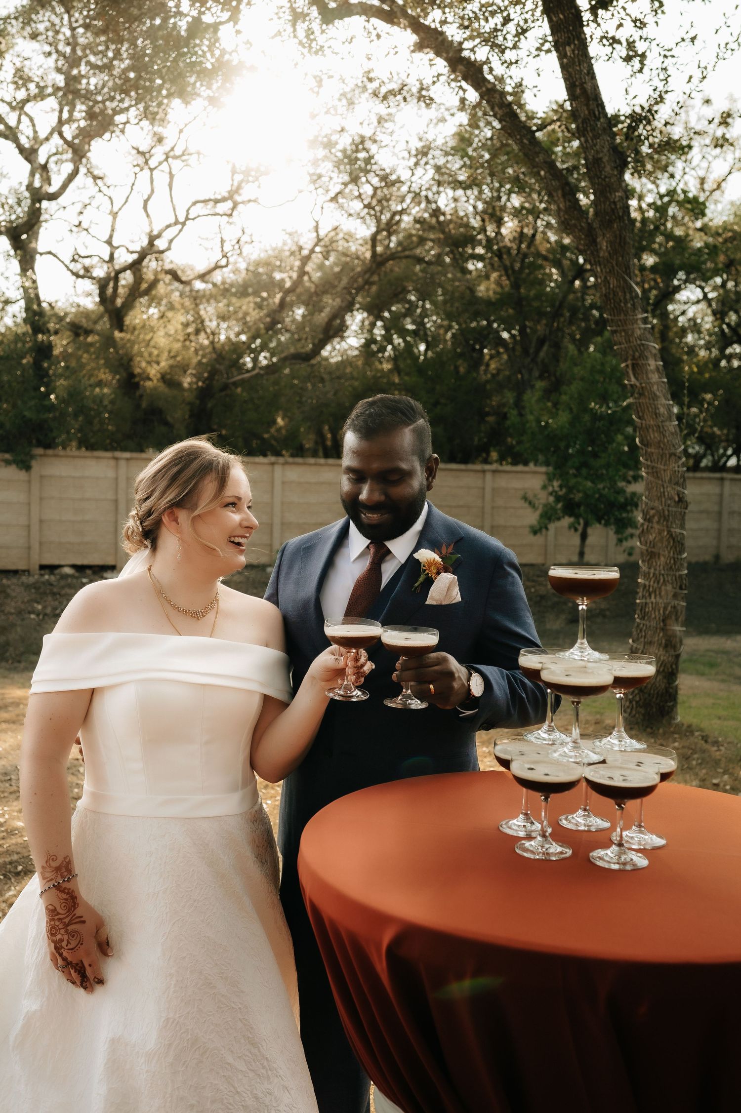 Newlyweds share champagne toast at outdoor reception with rustic decor.