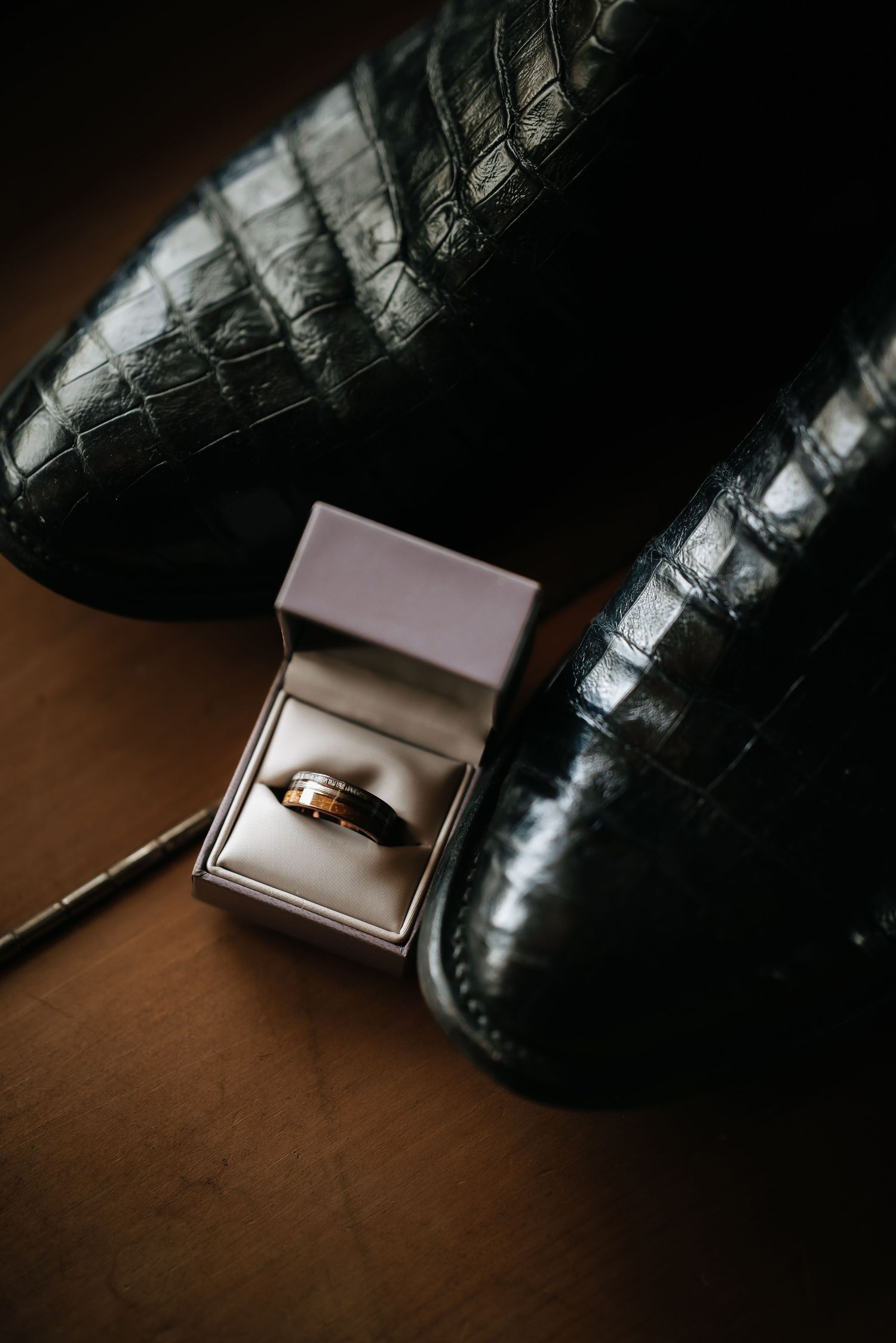 Wedding rings displayed in an elegant box next to formal black leather shoes.