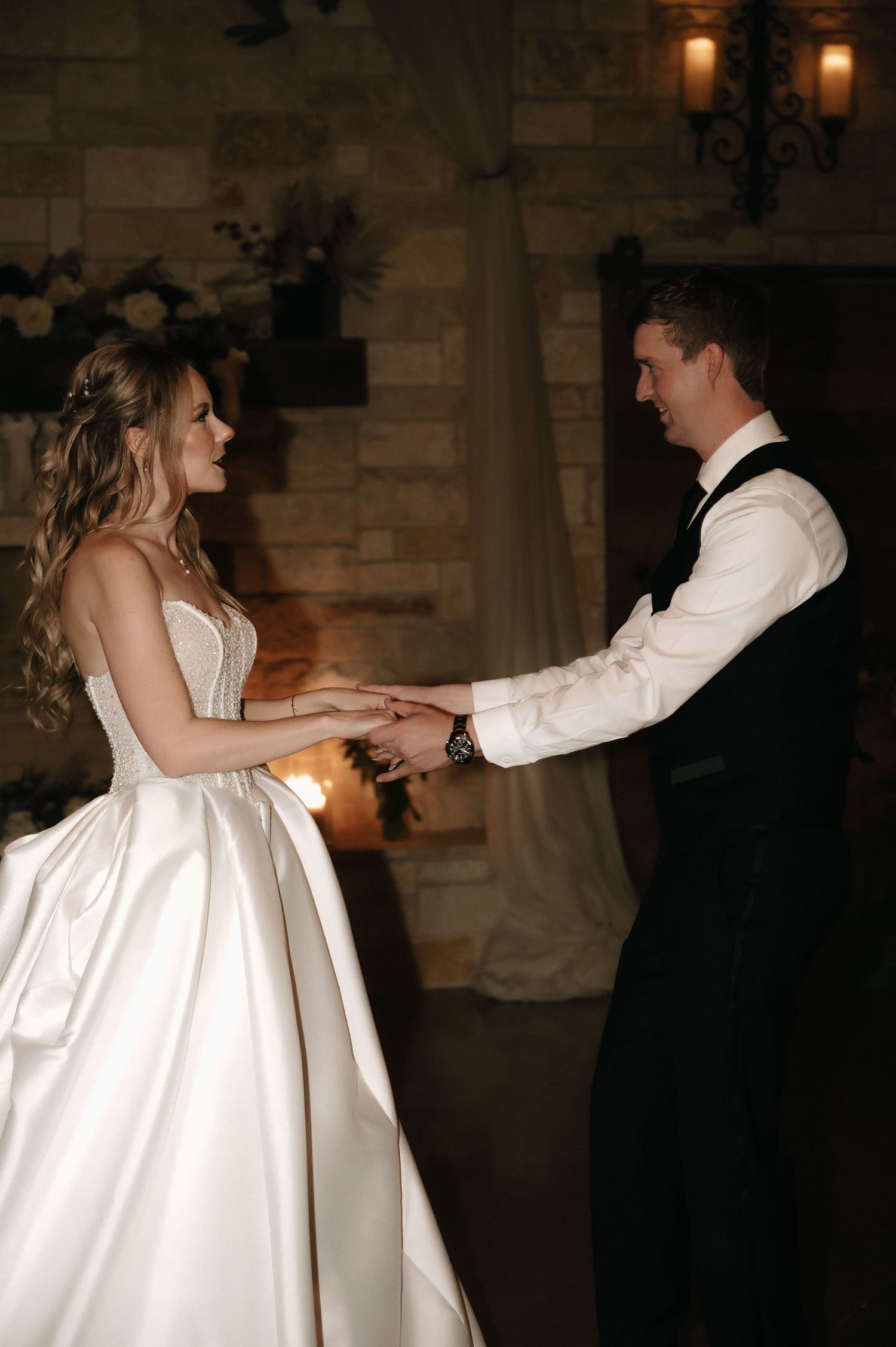 A couple performs their first dance in an elegant stone-walled venue with warm lighting.