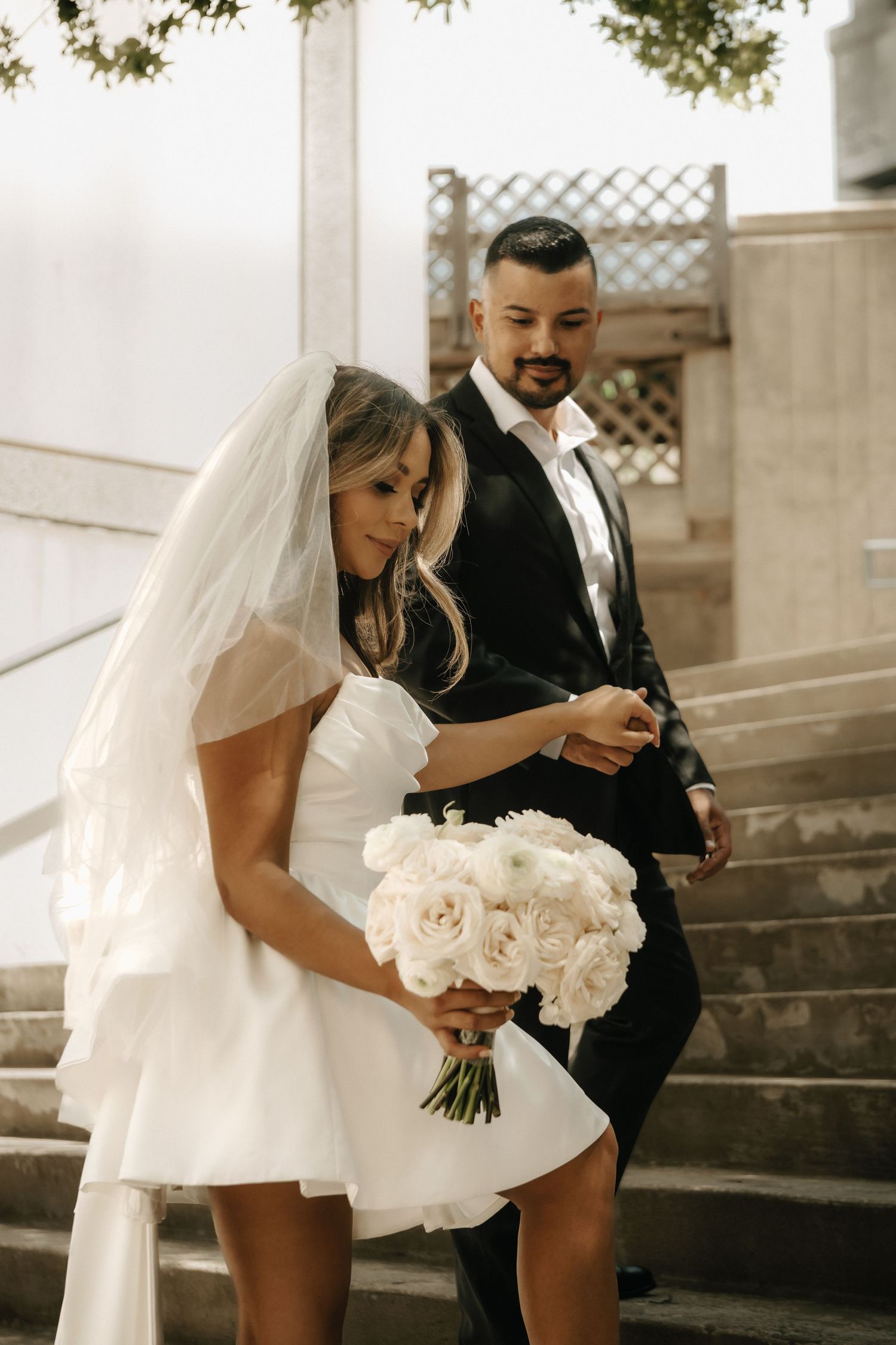 A couple shares a tender moment on stone steps with the bride holding white roses.