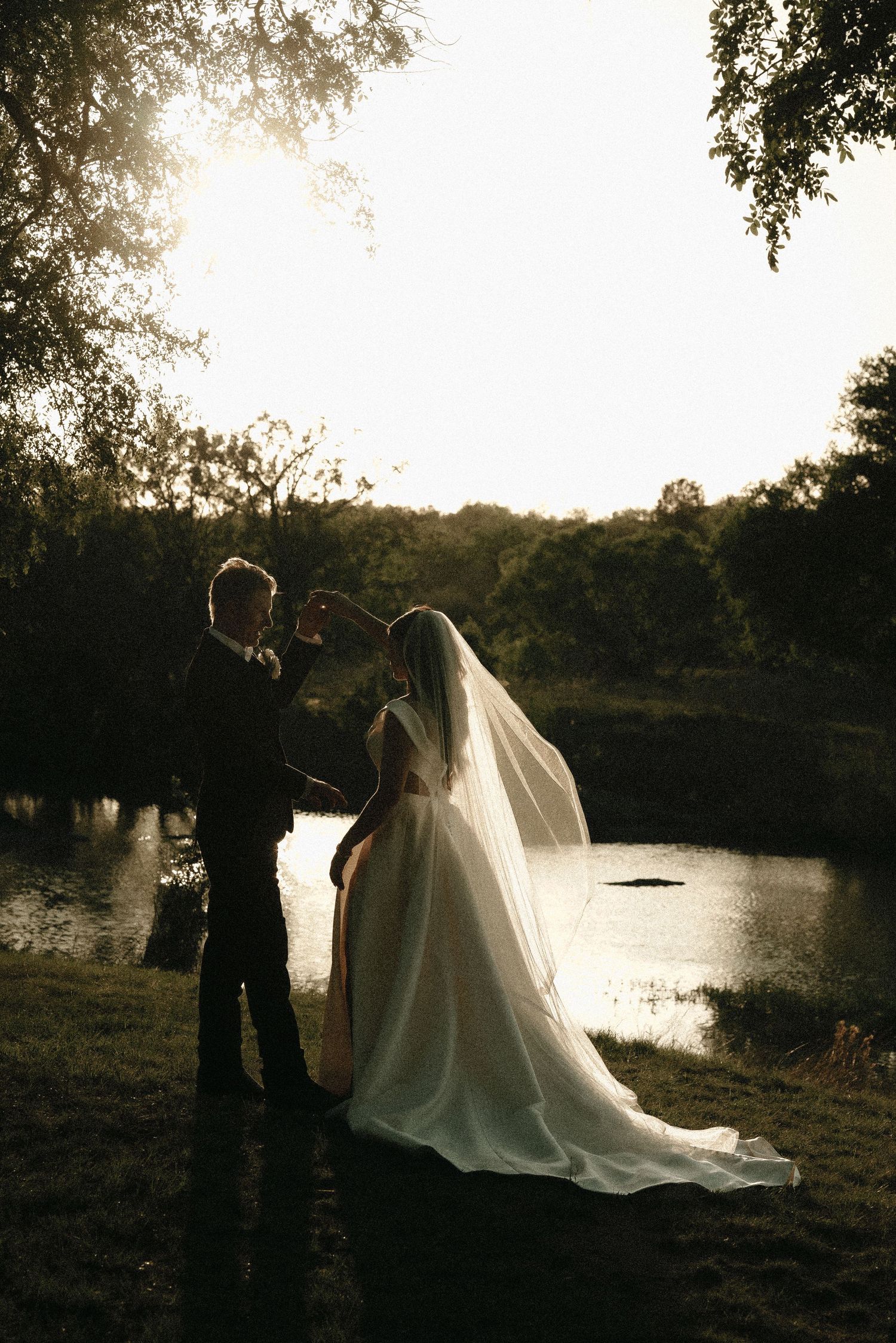 Silhouetted wedding couple by a lake during golden hour sunset.