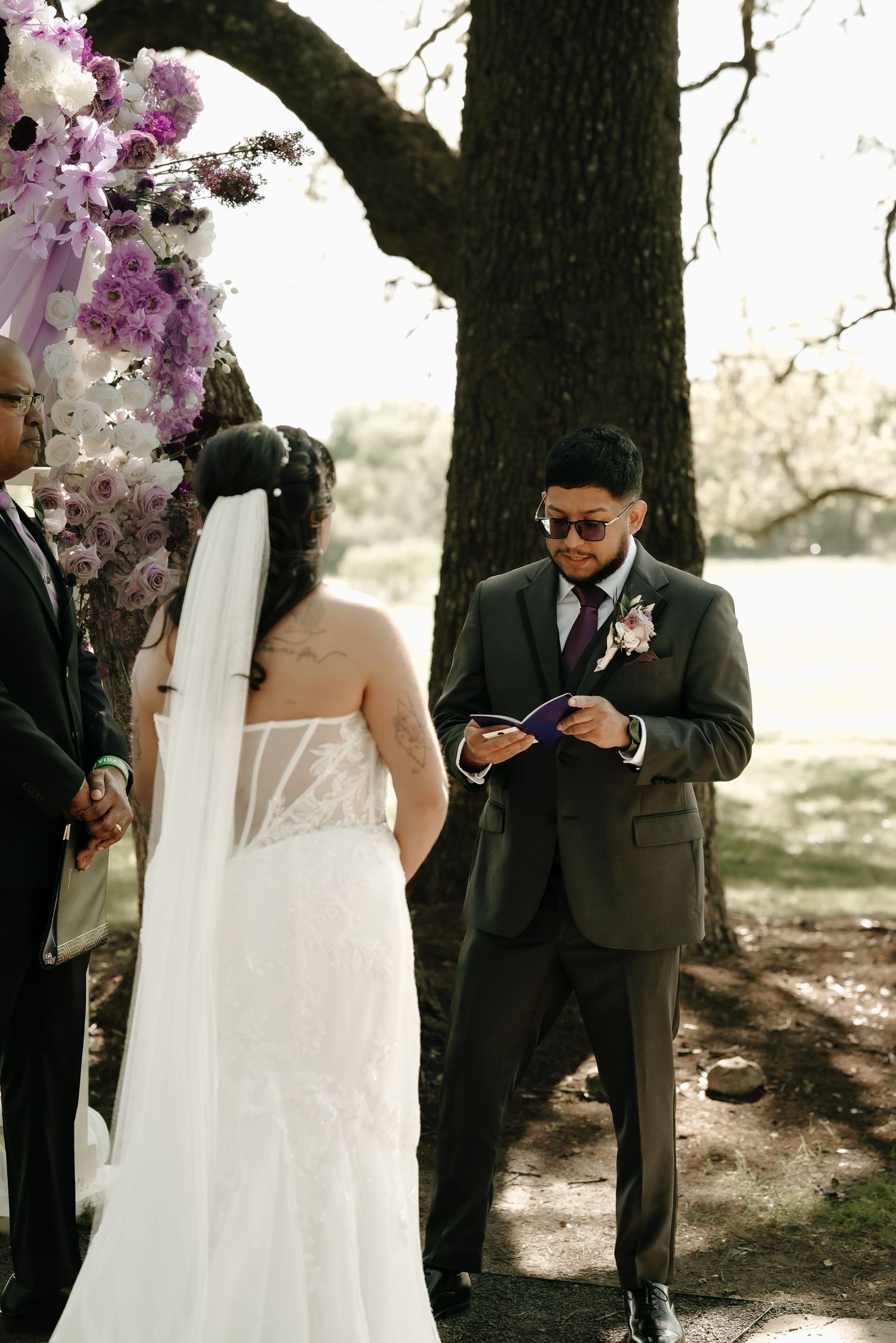 Wedding ceremony setup with purple floral decorations under large oak trees.