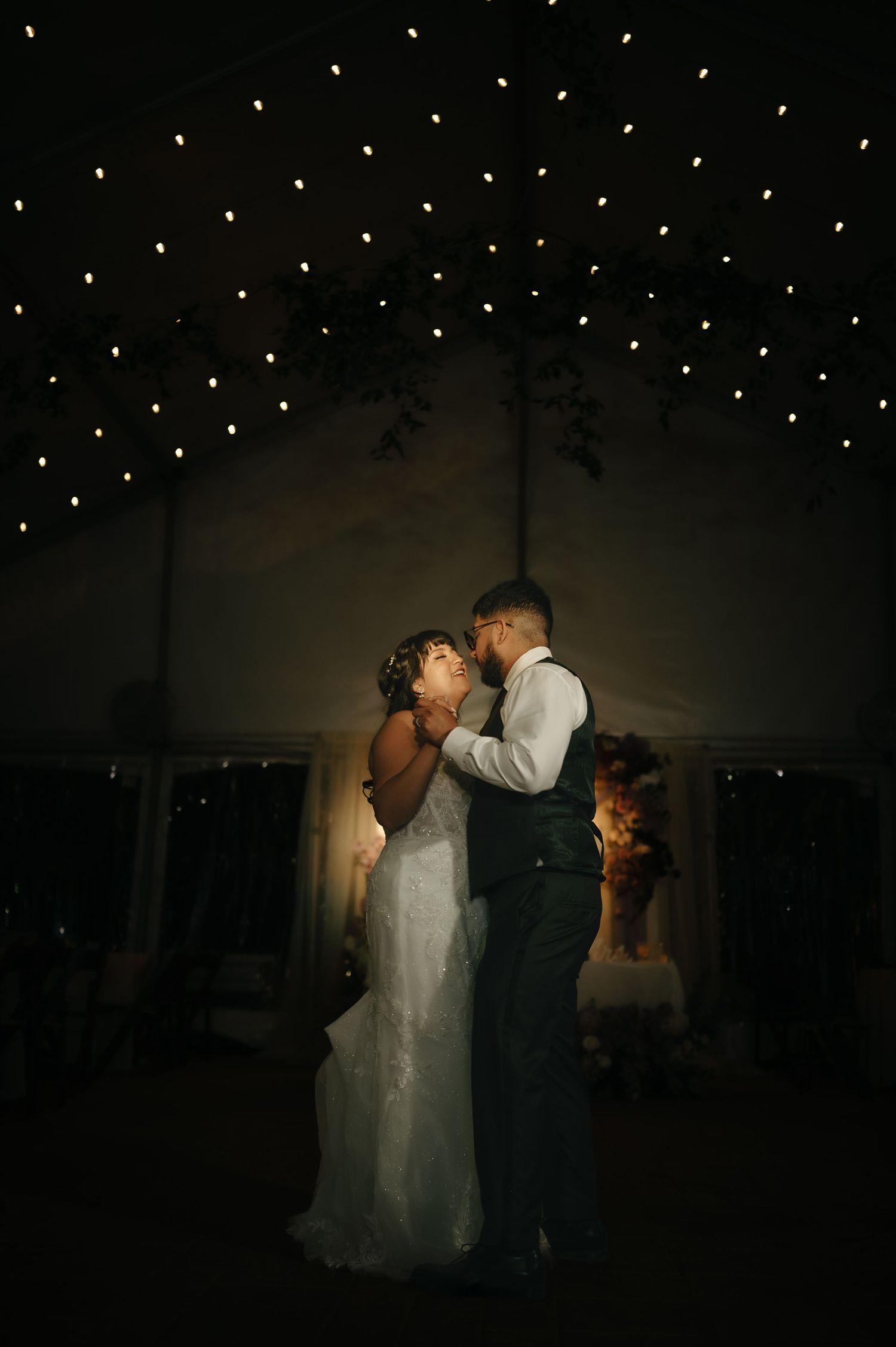 Romantic dance sequence under twinkling lights in a dark reception venue.
