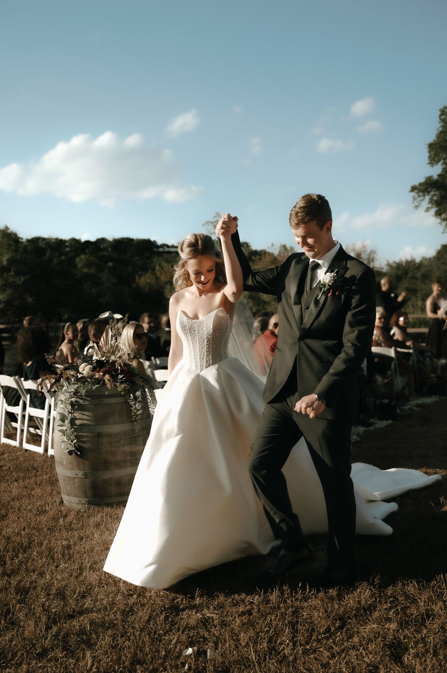 Joyful wedding couple celebrates during outdoor ceremony with guests in background.