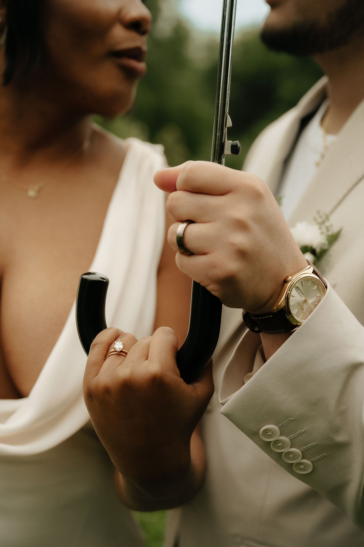 Close-up of bride and groom holding umbrella handles, showcasing wedding rings and gold watch on their special day.