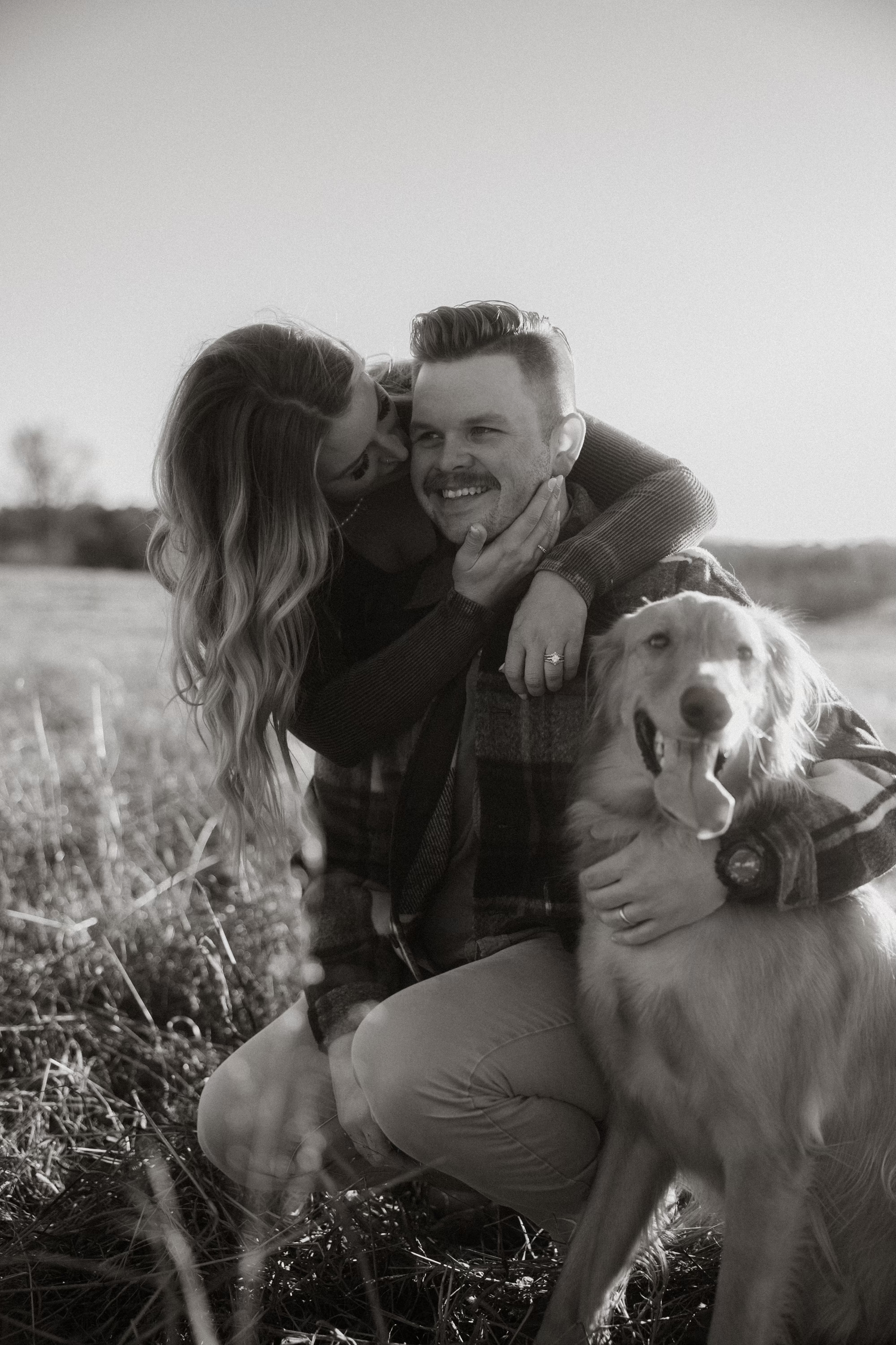 A couple and their dog share intimate moments in a sunny field.