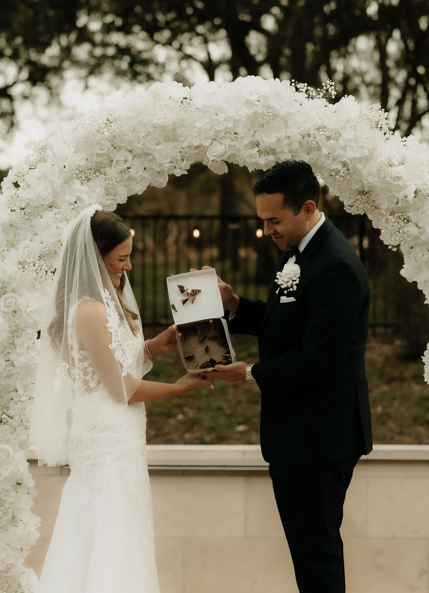 Couple shares a moment under a stunning white floral arch during their outdoor wedding ceremony.
