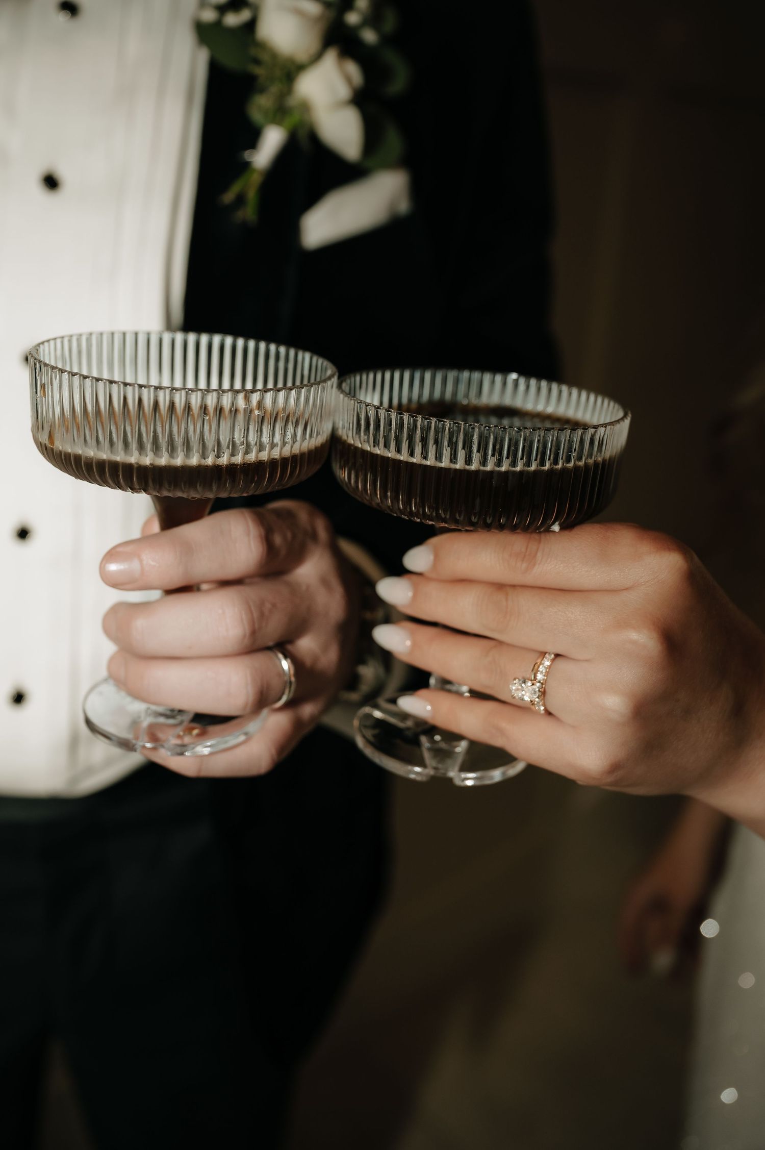 Close-up of wedding rings and champagne glasses held by couple in formal attire.