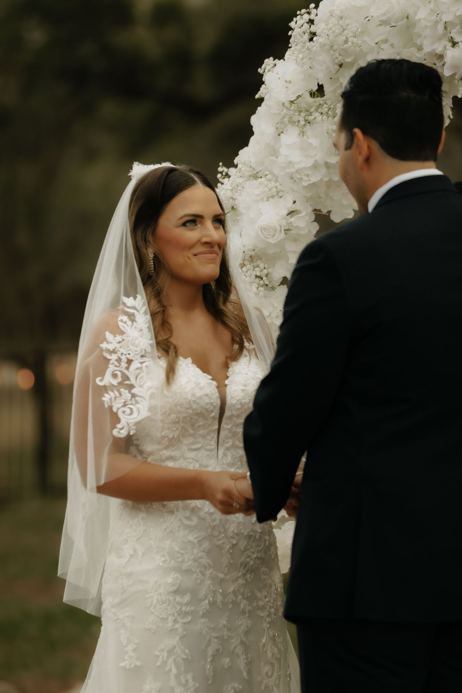 Beautiful outdoor wedding ceremony with couple standing beneath an elaborate white floral arch.