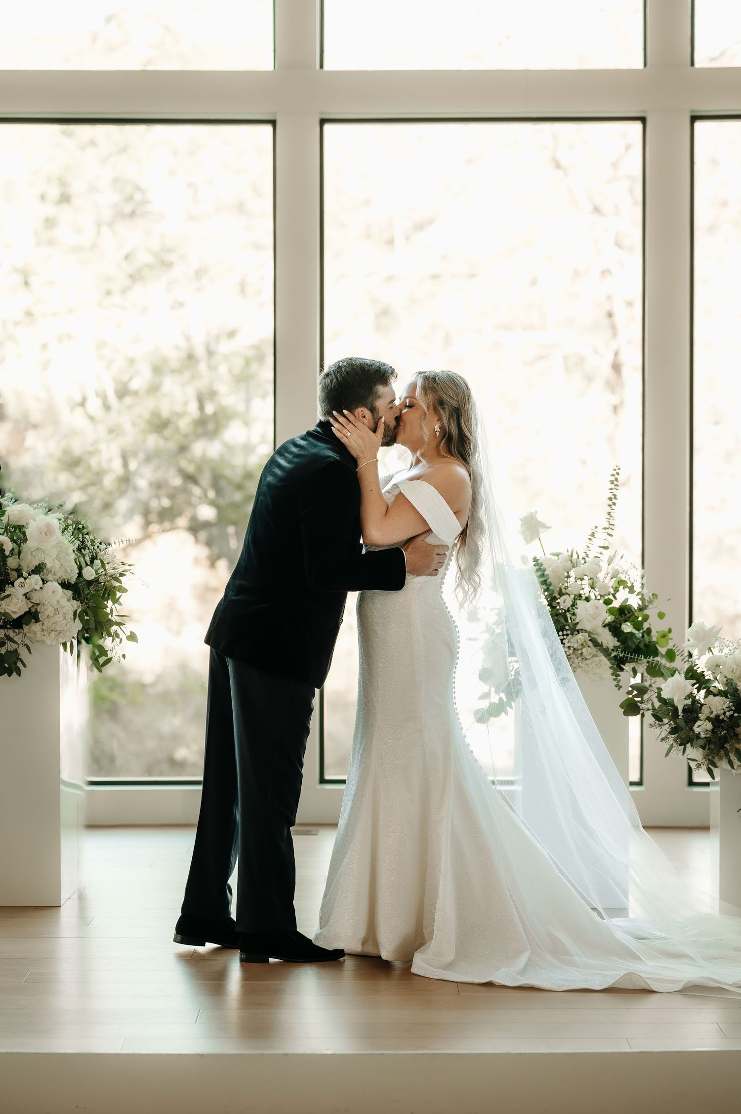 Tender wedding moment captured against large windows in a light-filled modern venue.