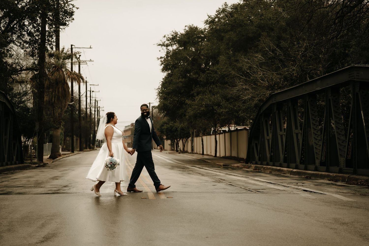 Wedding couple walking along a tree-lined path in sepia tones creating a romantic vintage atmosphere.