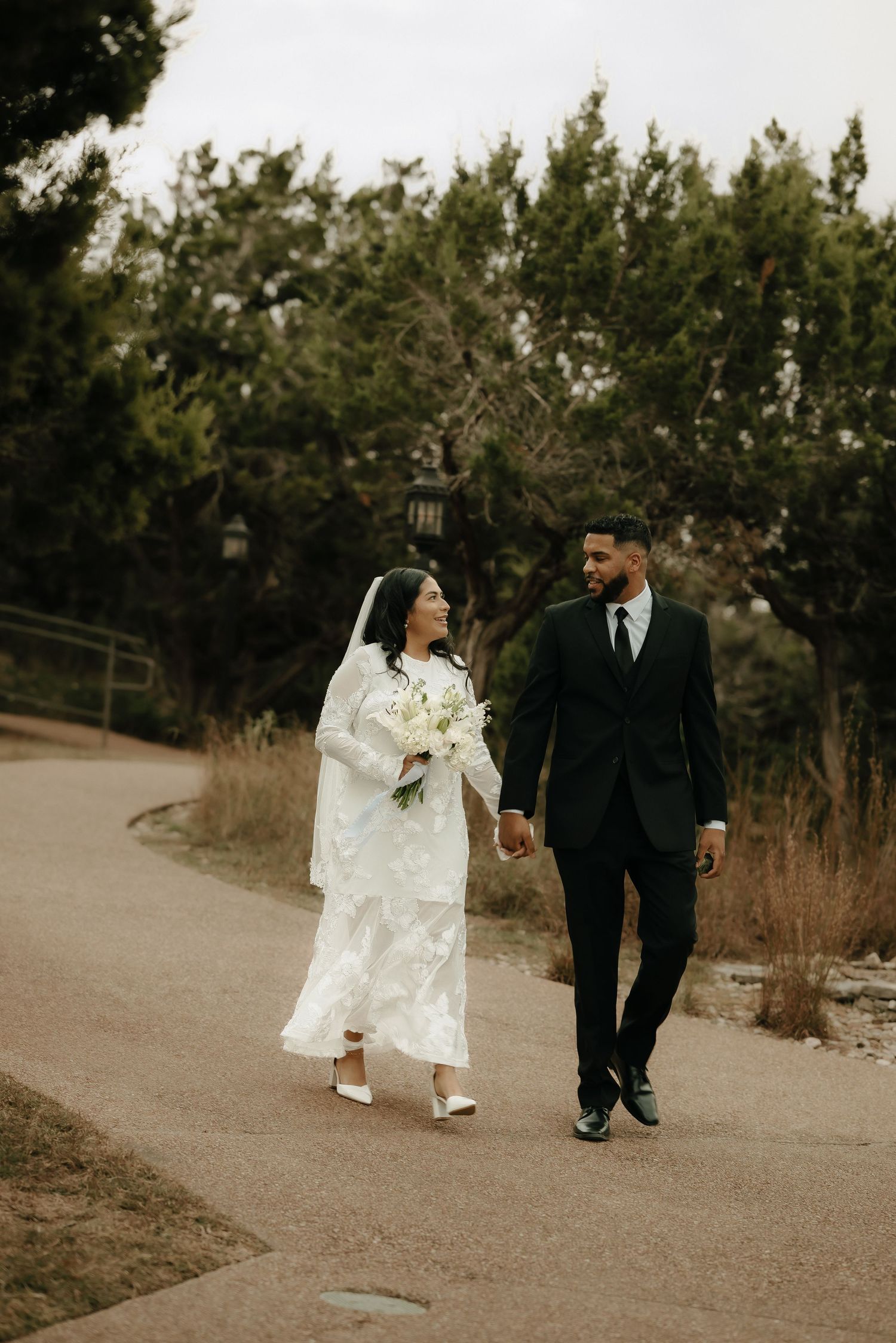 Wedding couple walking together on a path surrounded by greenery.