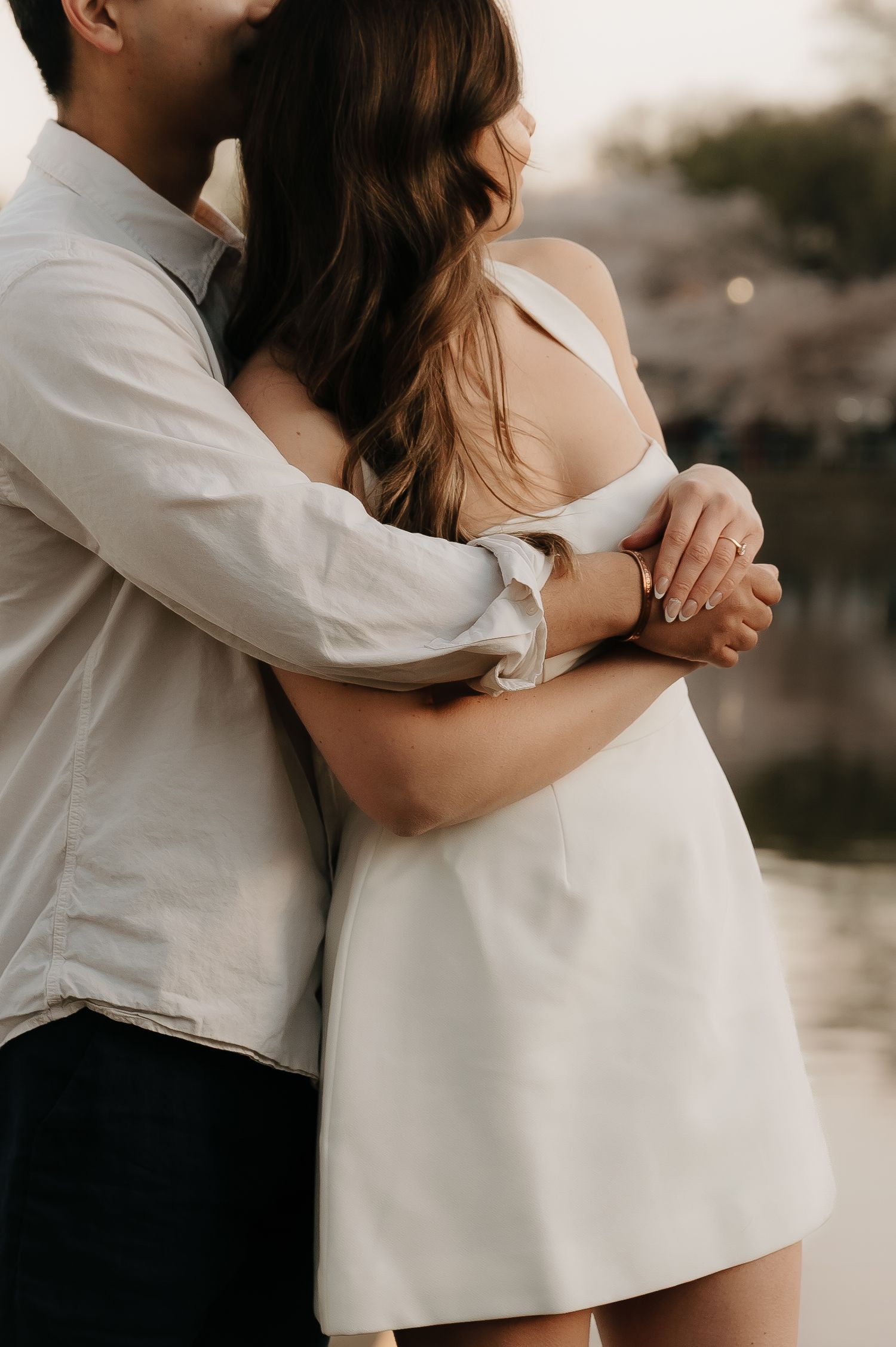 Couple embracing tenderly near a waterfront, woman in white mini dress with man in light blue shirt holding her close.
