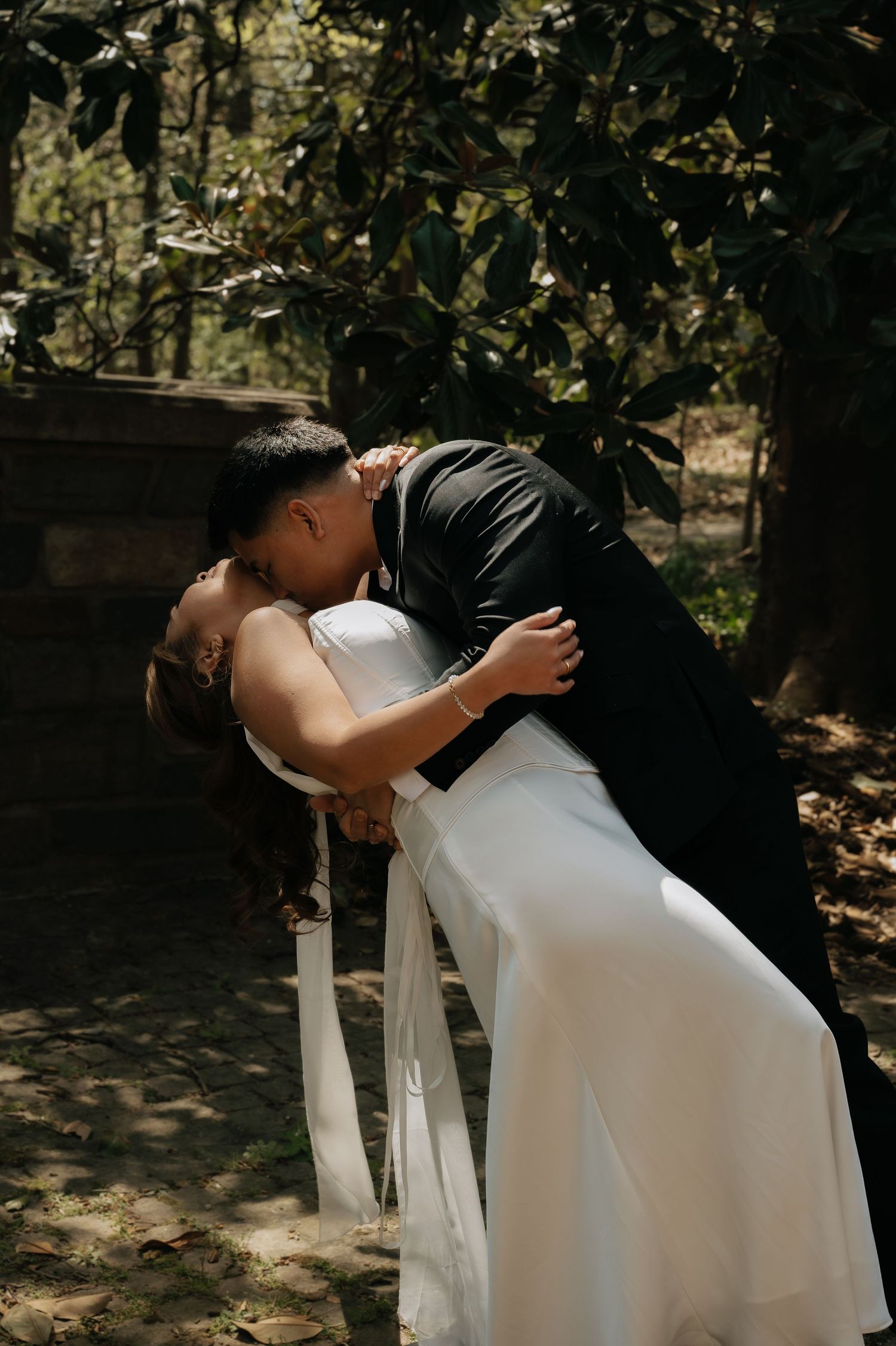 Groom dips bride for a romantic kiss outdoors, bride wearing elegant white wedding gown.