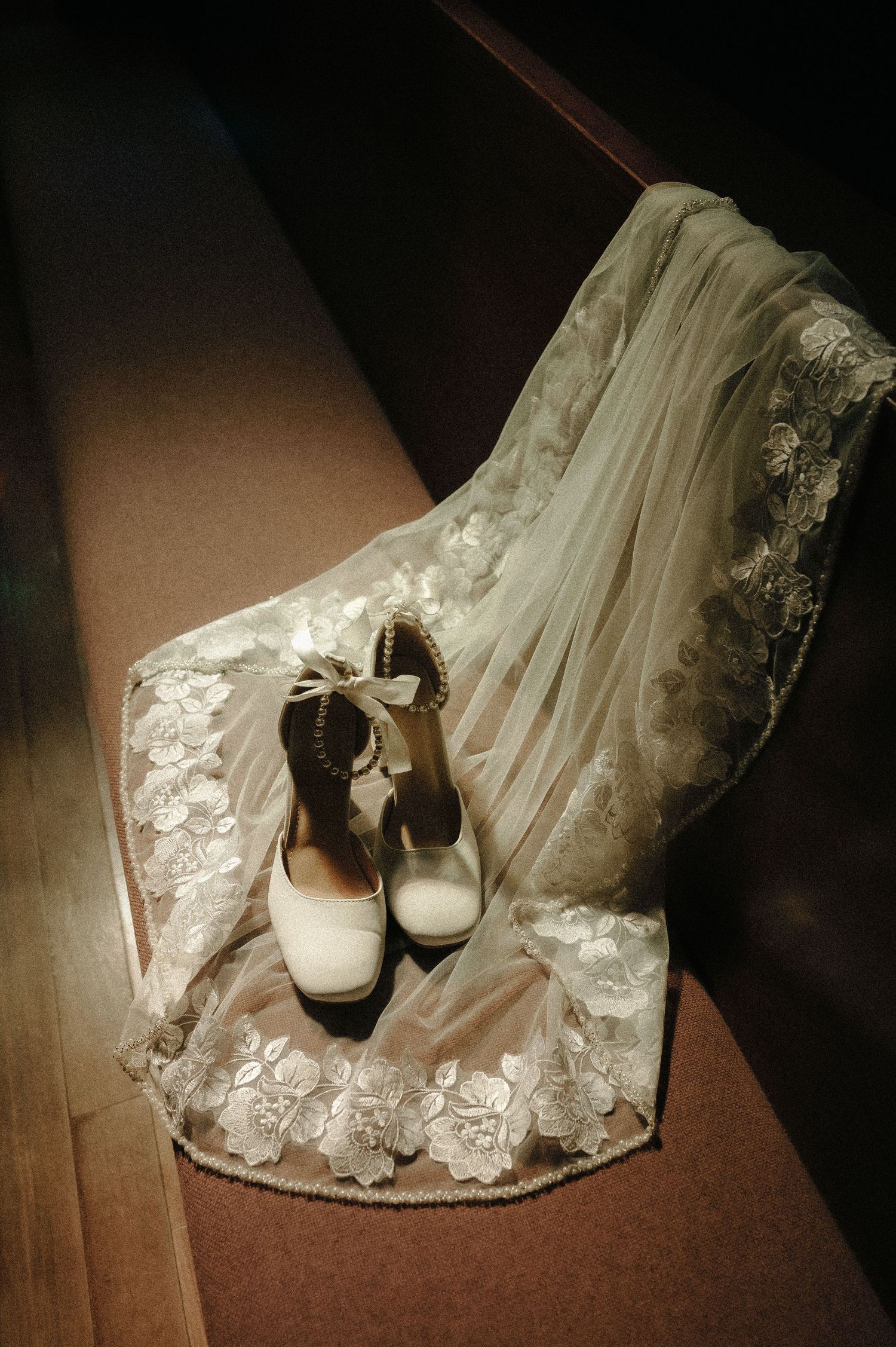 White lace wedding dress hem with classic bridal shoes on dark floor.