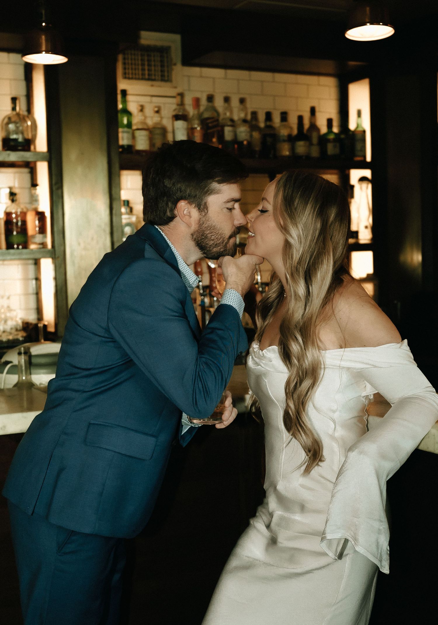 Romantic moment between couple sharing a kiss at an elegant bar with backlit bottles.