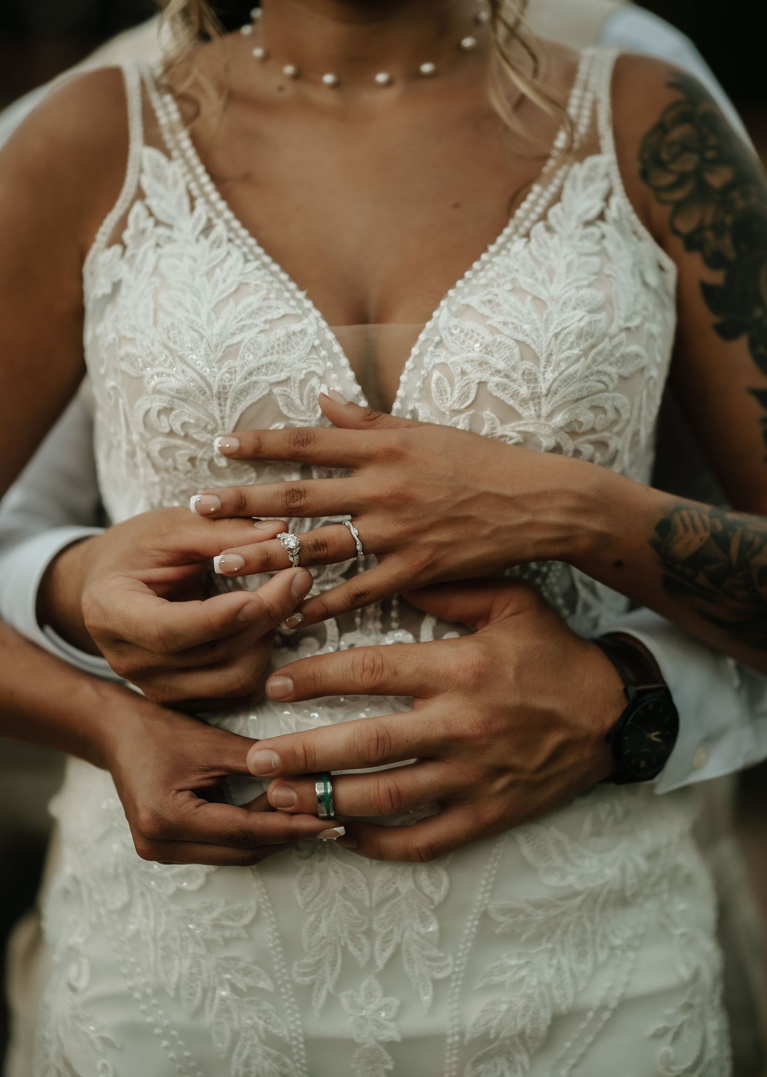 Close-up of hands with wedding rings against intricate lace wedding dress details.