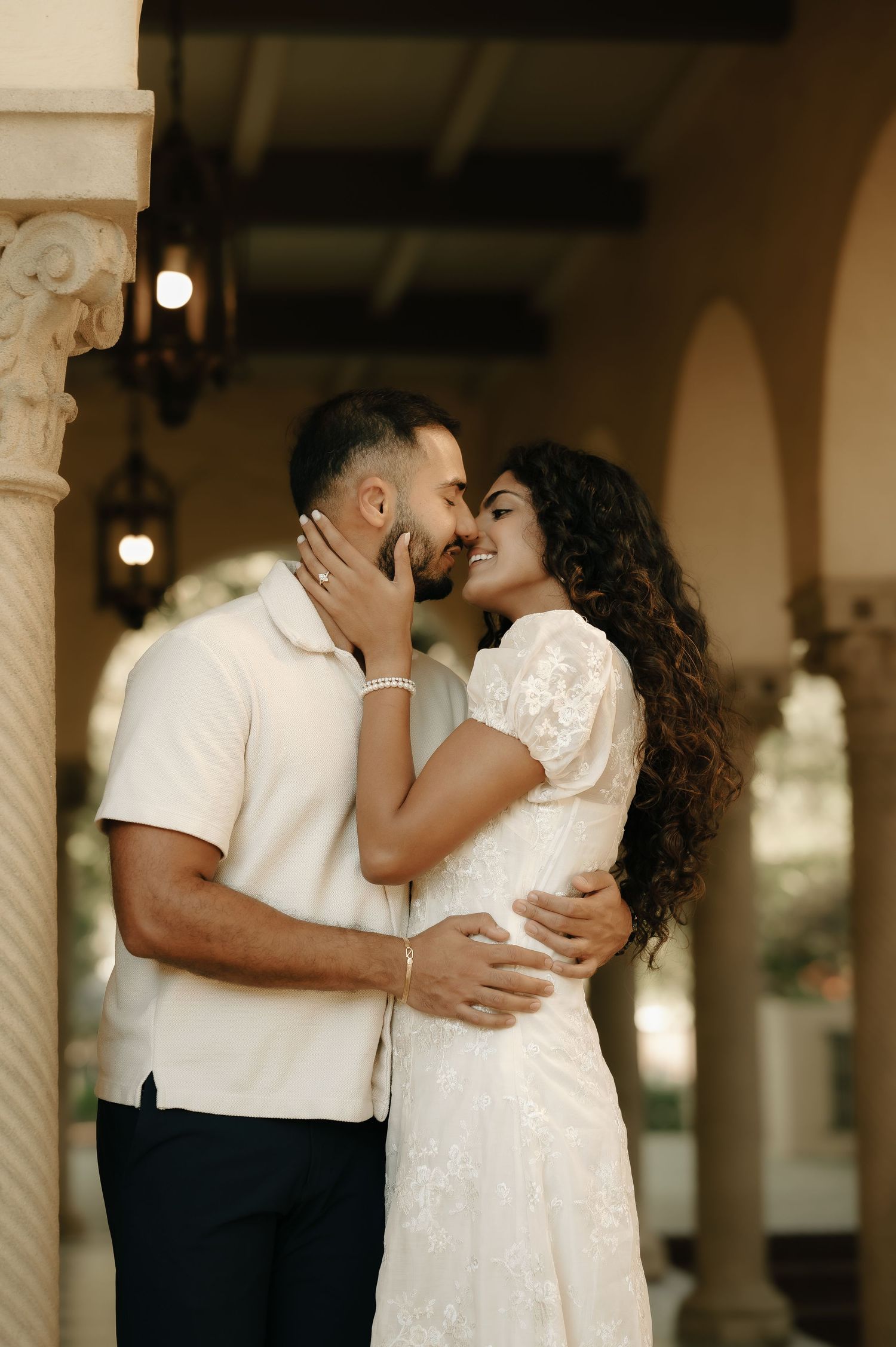 Romantic couple sharing an intimate moment in an elegant archway with decorative columns.