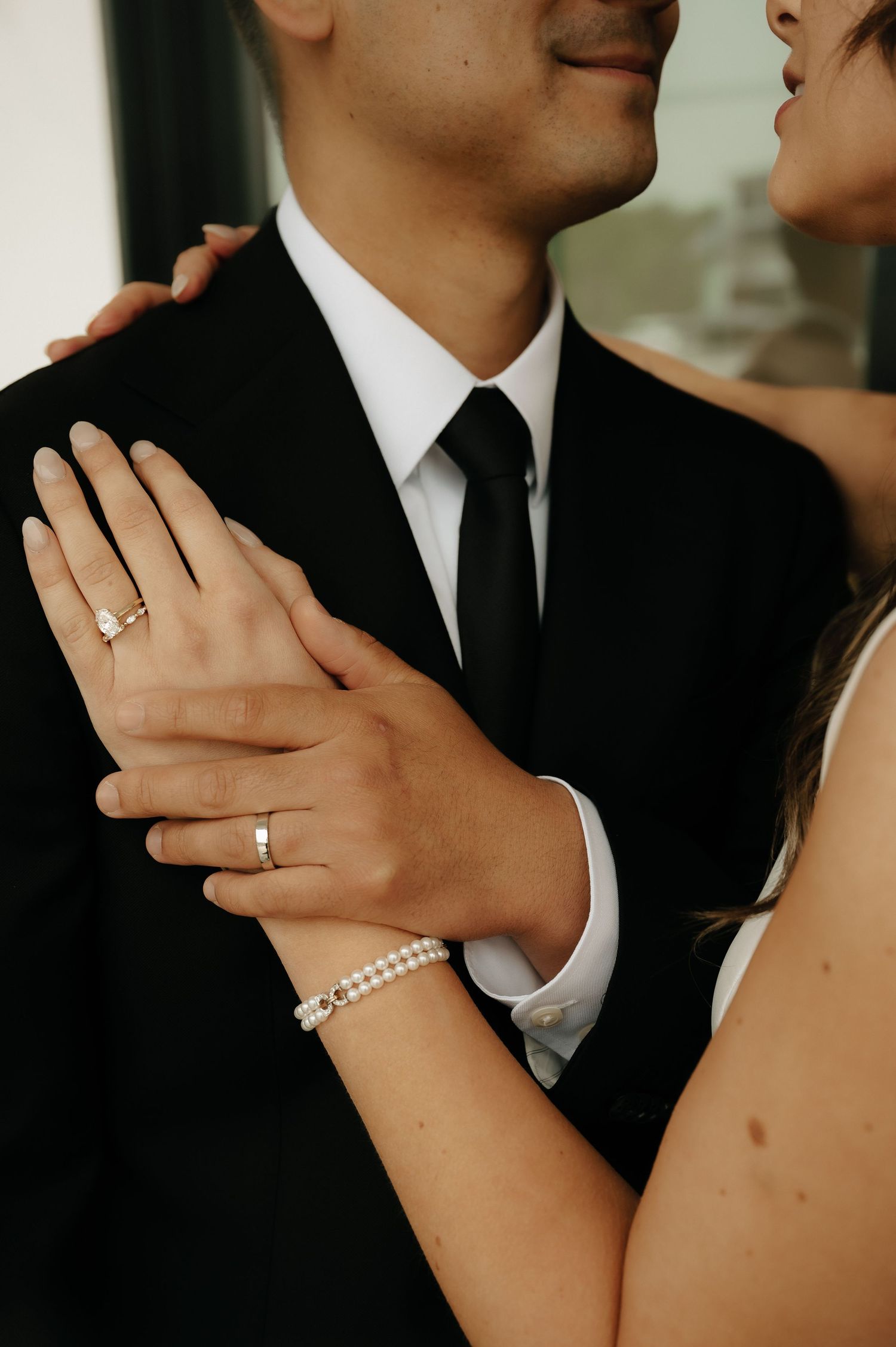 Bride and groom embrace, showcasing diamond engagement ring, wedding band, and tennis bracelet on her wrist.