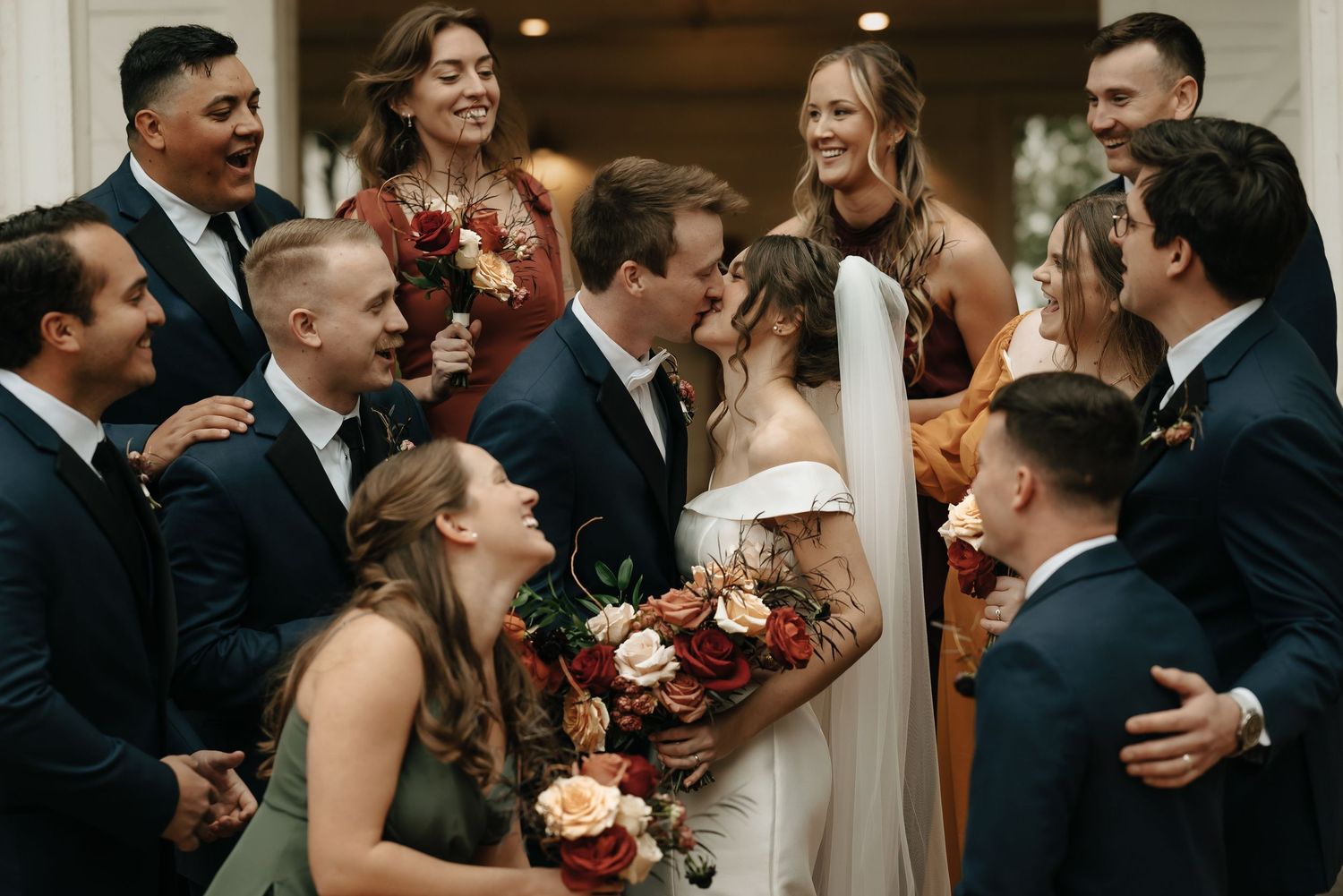 Wedding party celebrates joyfully together in formal attire with autumn-colored bouquets.