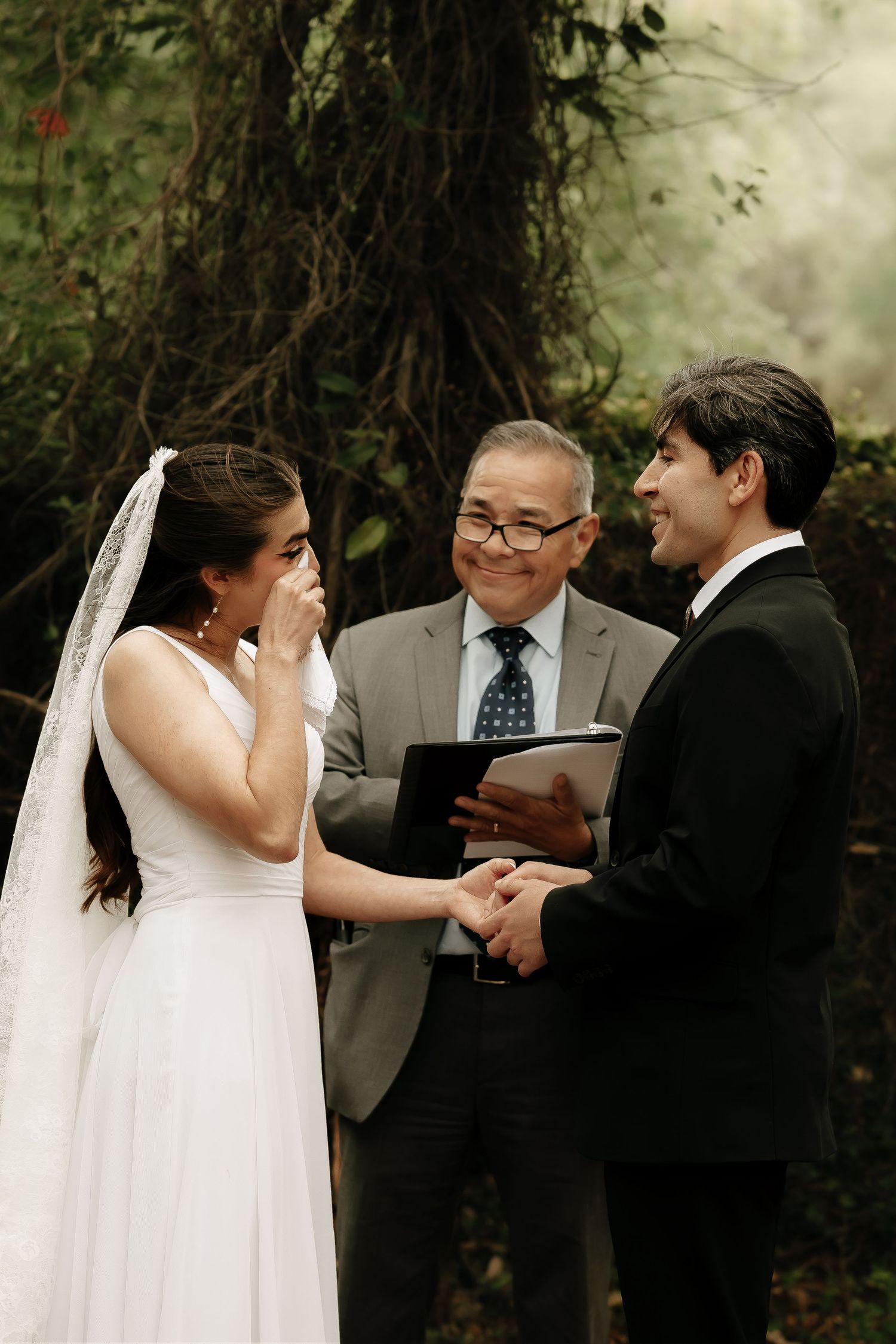 Wedding ceremony unfolds in a natural outdoor setting with elegant white decor.