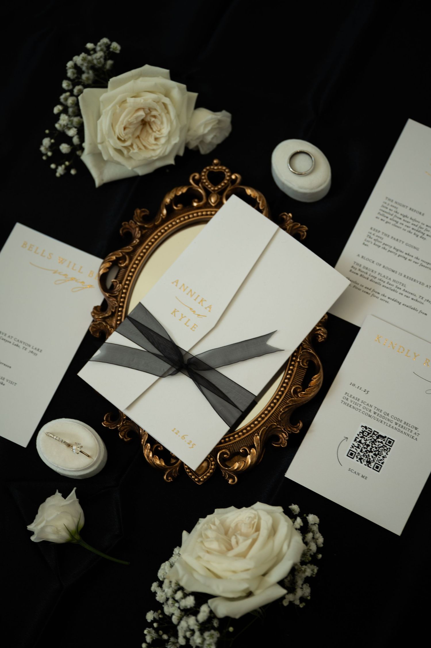 Wedding invitation suite with white roses and gold ornate frame on black background.