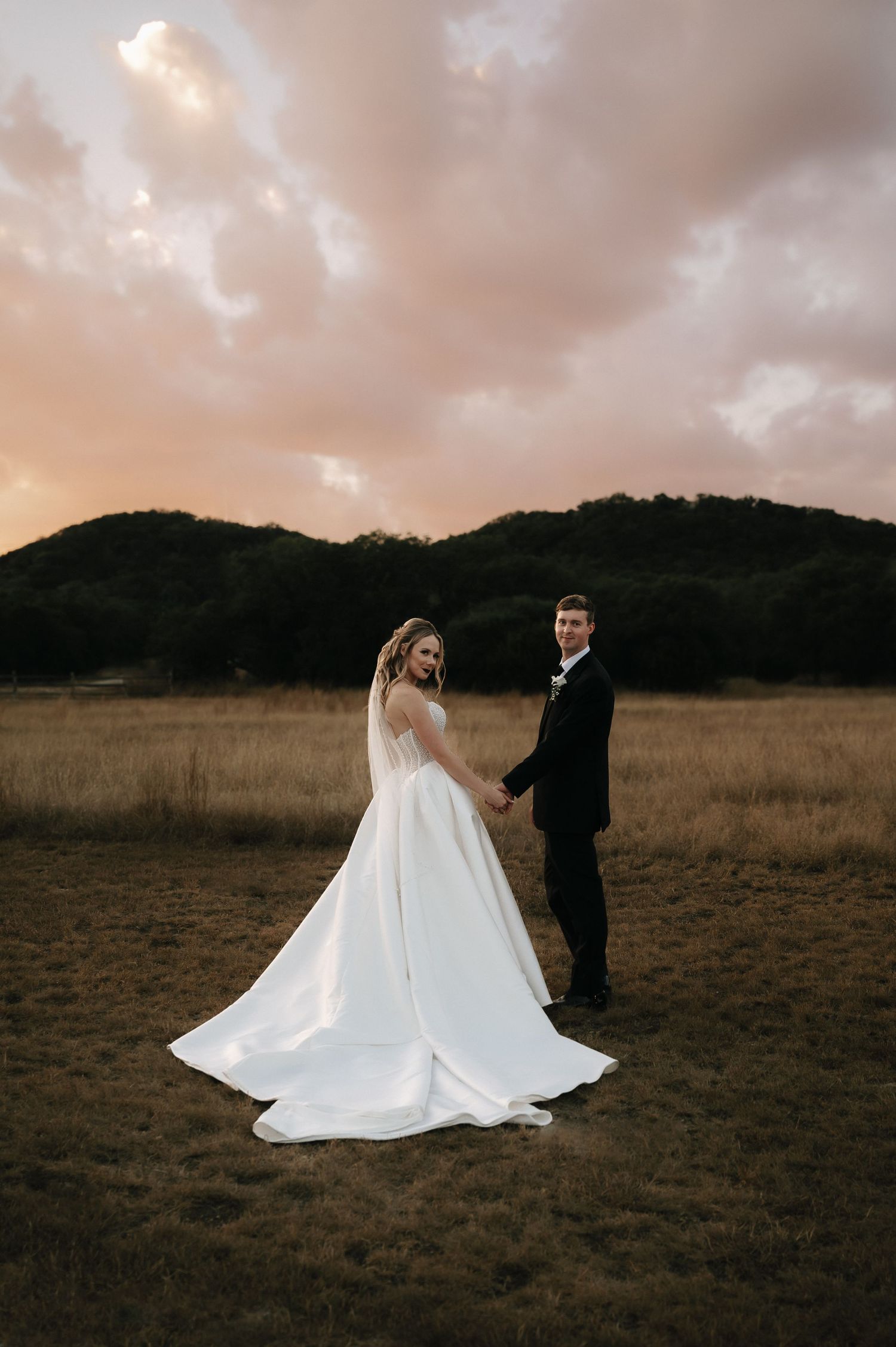 Couple poses in field at sunset with flowing white wedding dress.