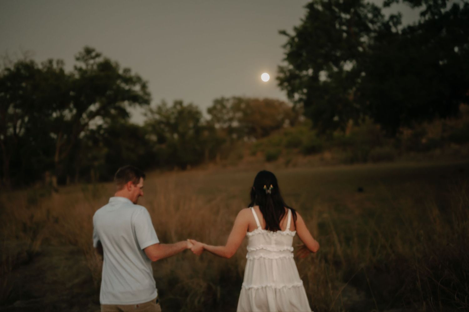 Couple holding hands while walking along a serene waterfront at dusk.