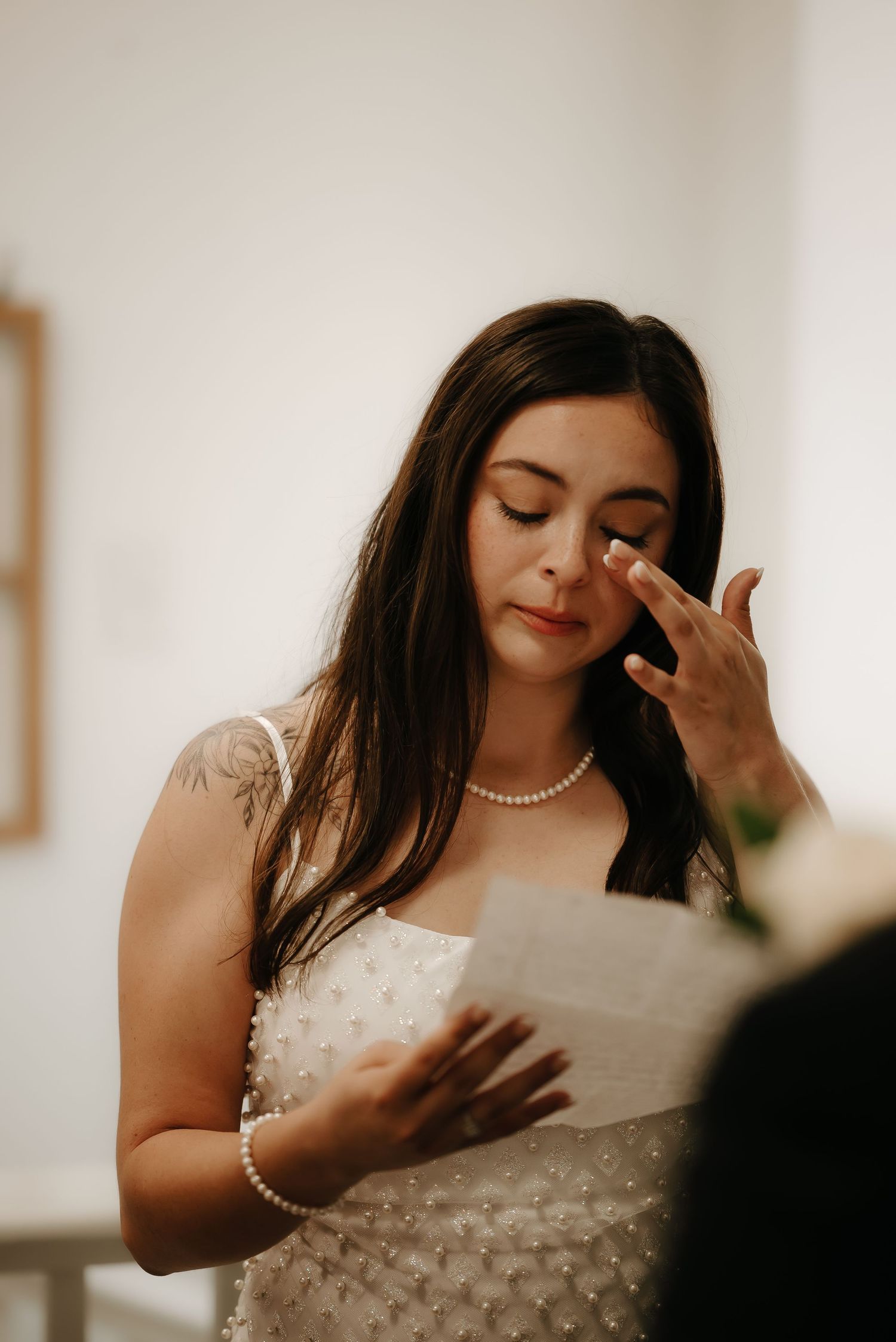 Emotional moment reading letter while wearing pearl necklace and white dress.