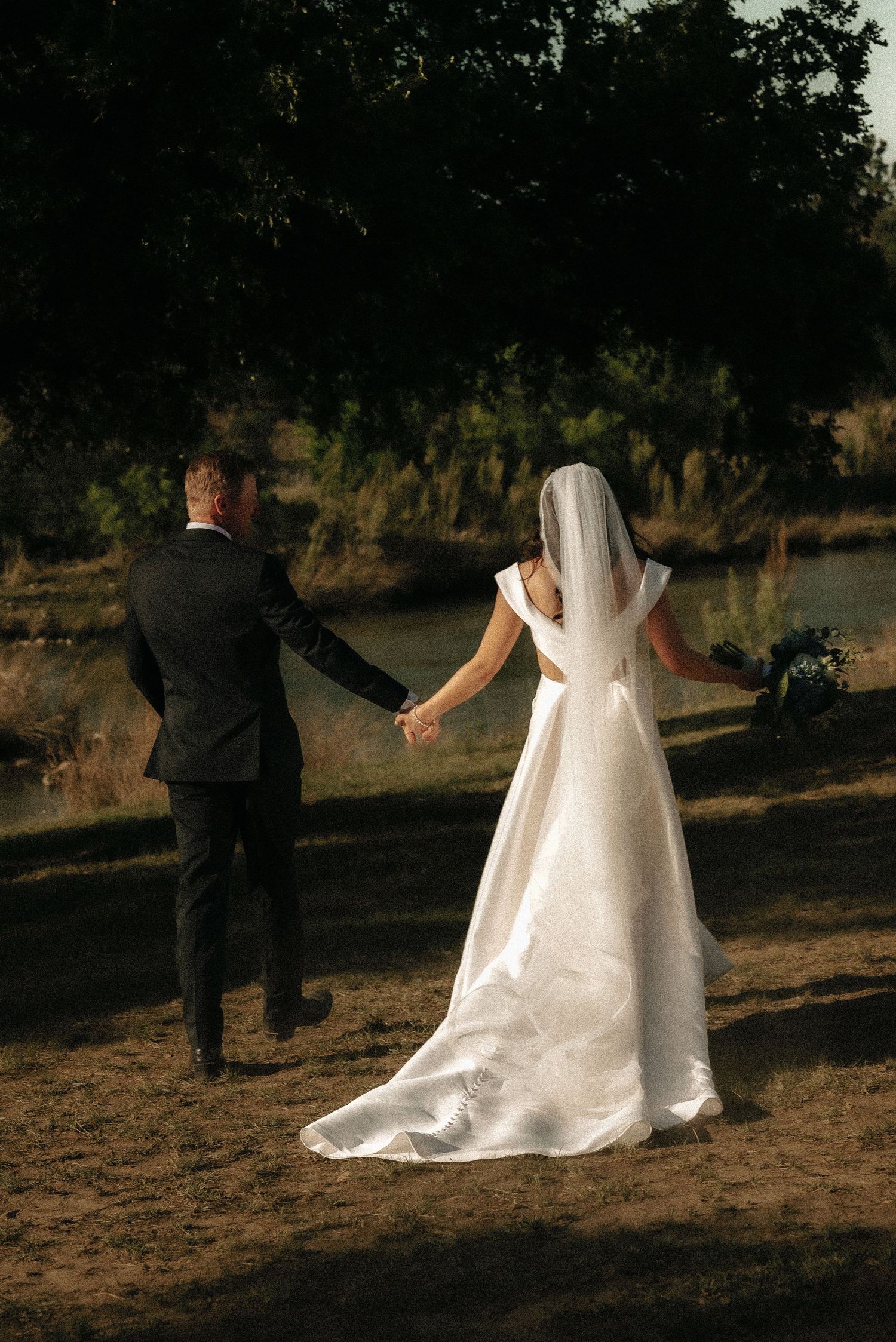 Silhouettes of wedding party walking through sunlit outdoor setting.