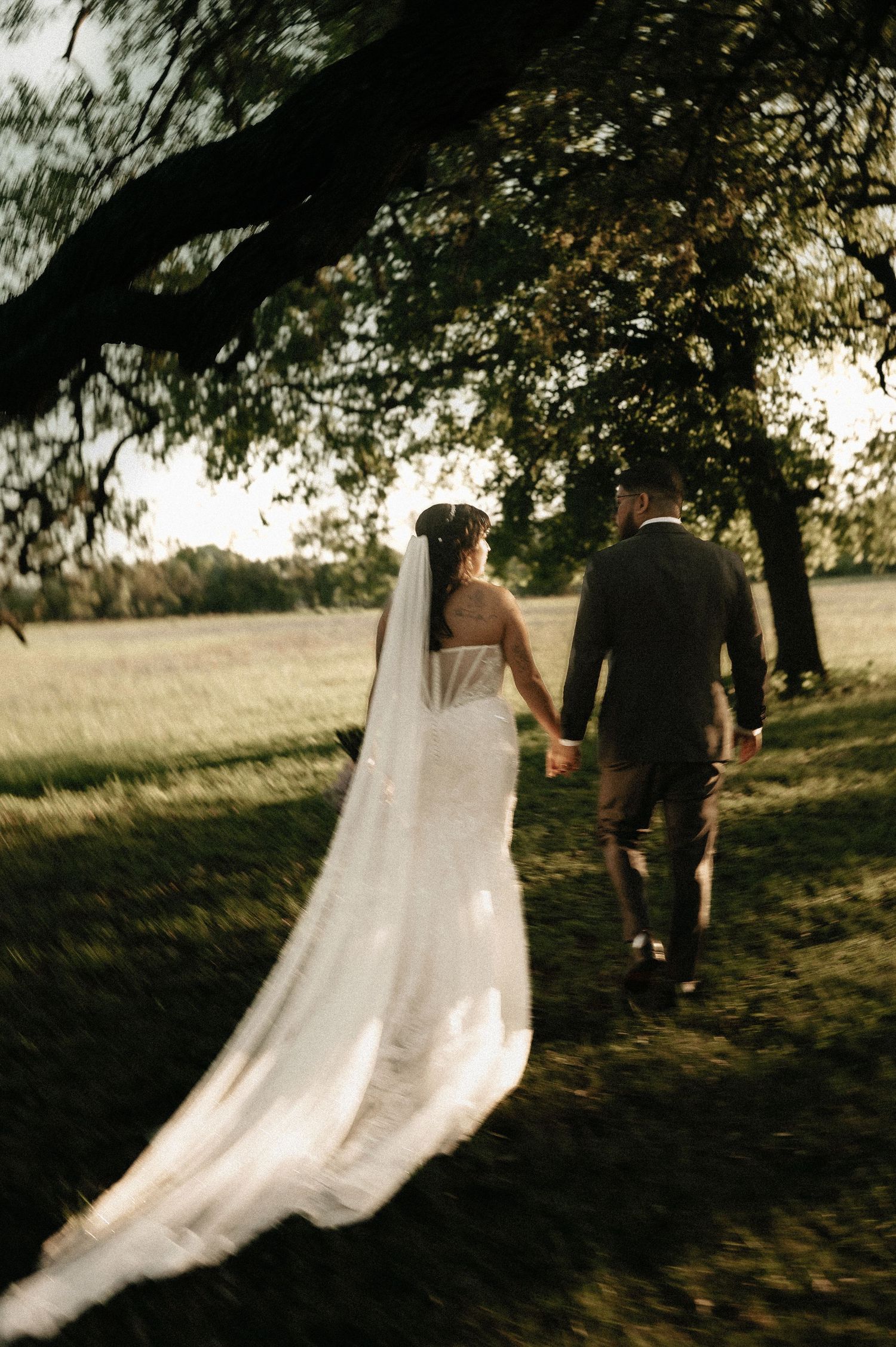 Sunset wedding portrait with flowing bridal train trailing behind couple.