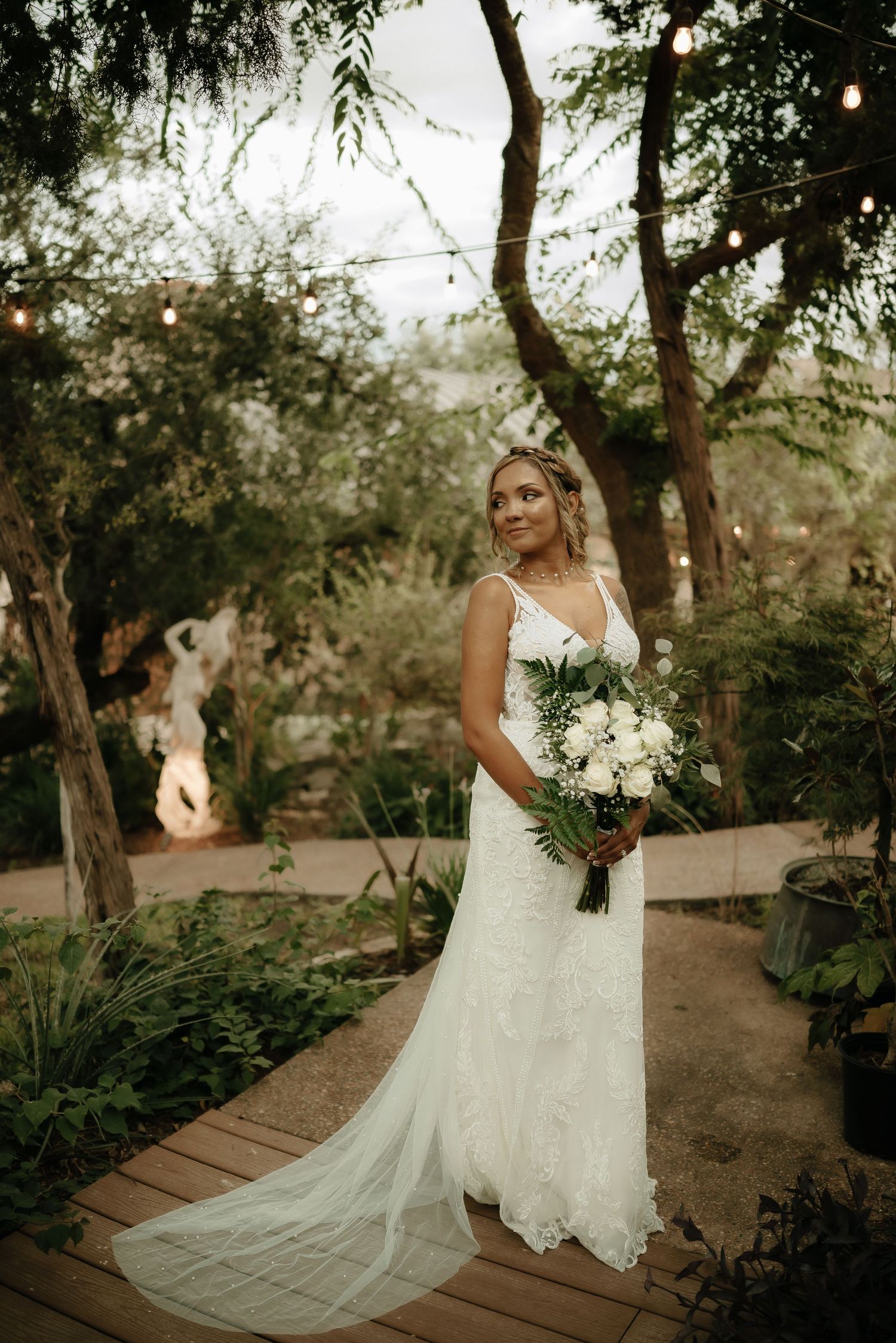 Elegant bridal portrait on wooden pathway surrounded by lush garden greenery.