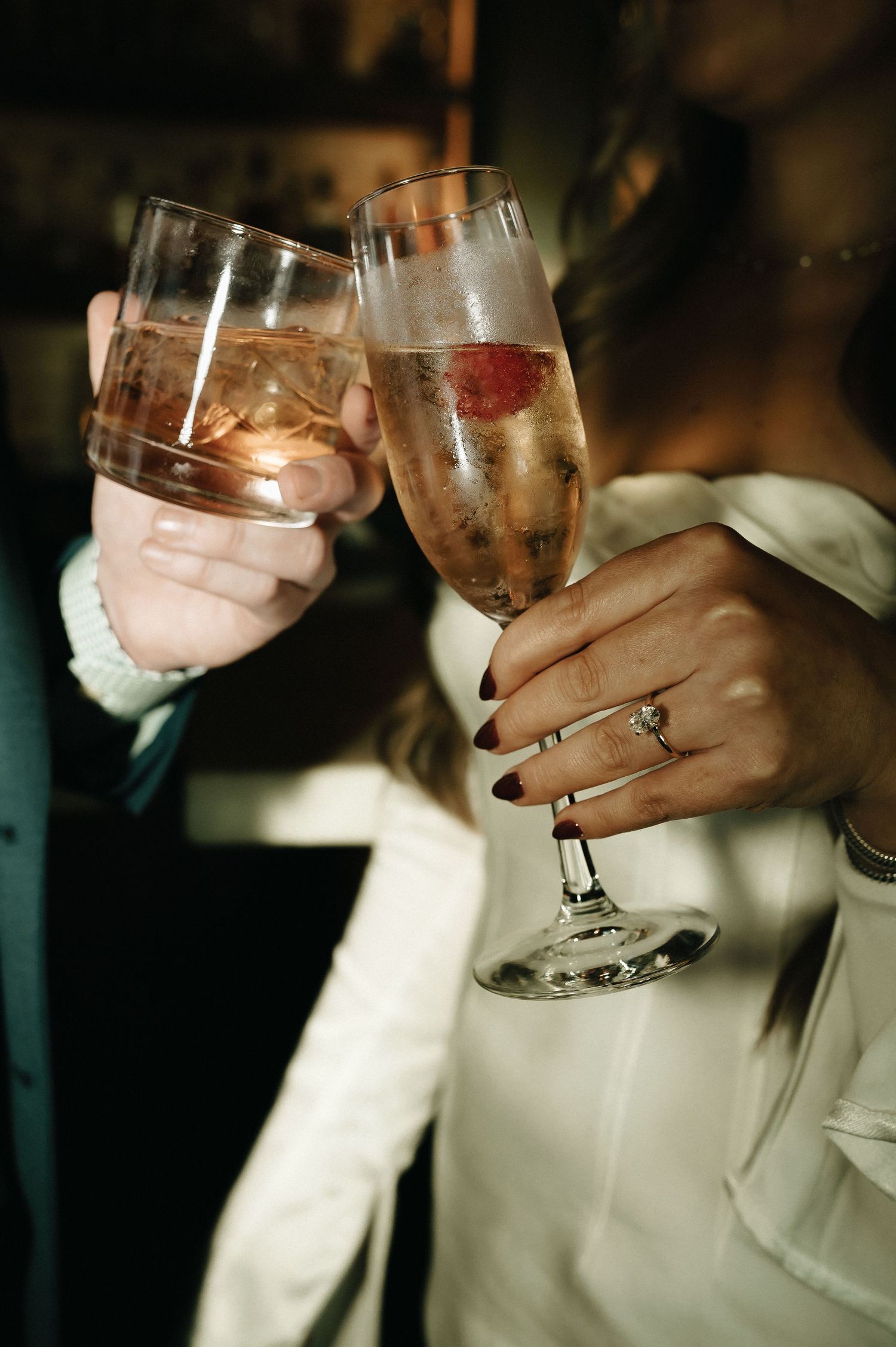 Champagne toast with elegant glasses showing engagement ring detail.