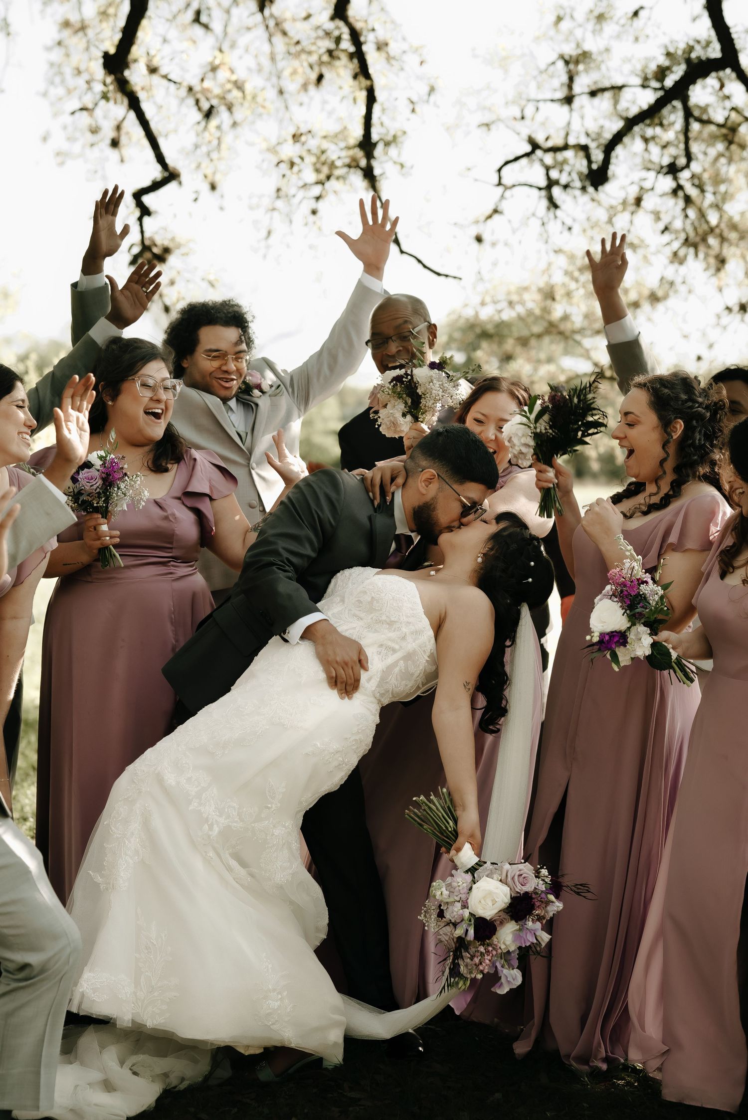 A joyful wedding party celebrates with energetic poses in mauve bridesmaid dresses.