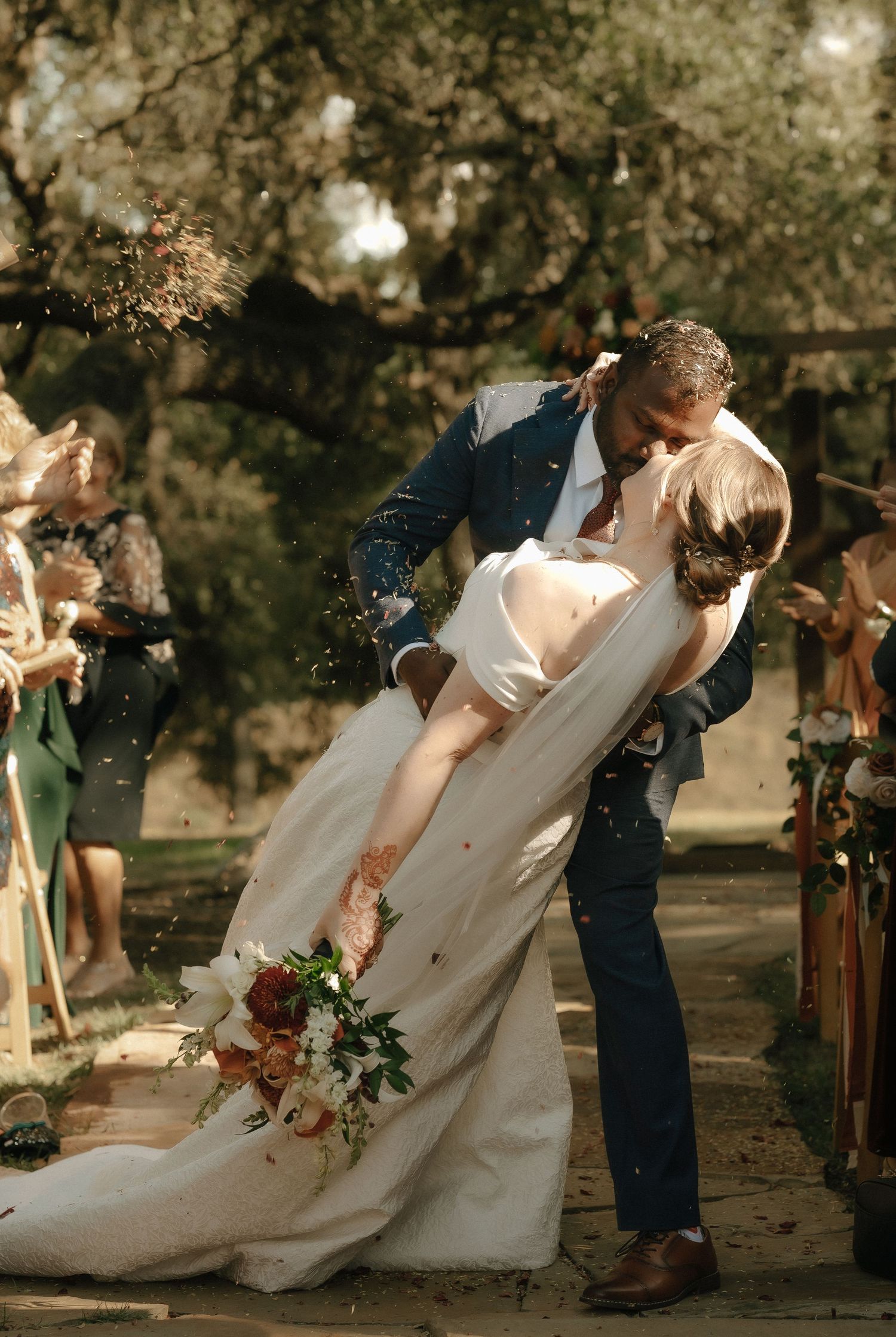 Romantic outdoor wedding ceremony shows couple sharing a dramatic dip kiss under trees.