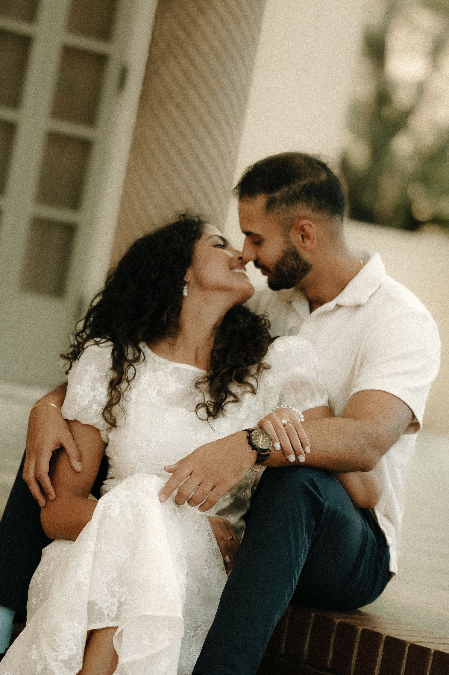 Intimate moment shared between couple sitting together against white architecture.
