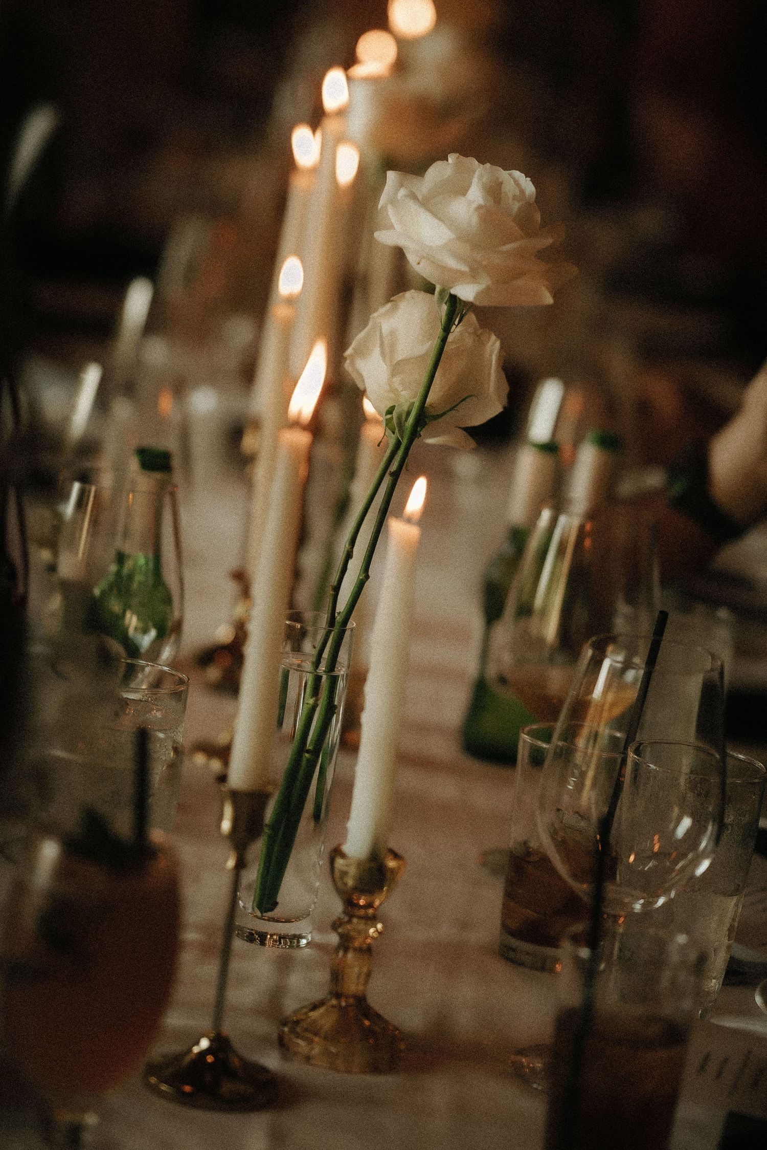 Romantic table setting with white roses in glass vases and glowing candles.