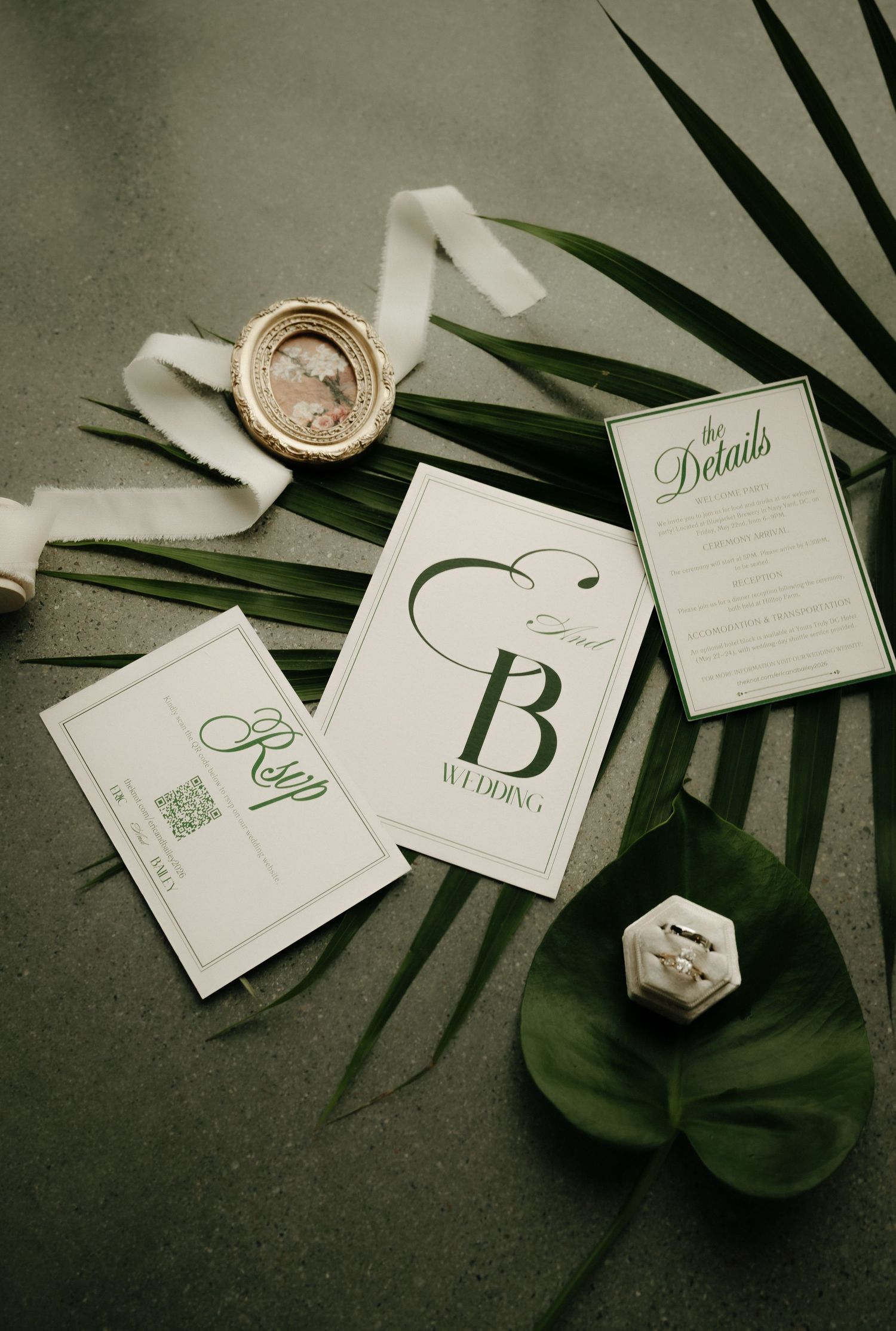 Elegant wedding stationery suite with green botanical accents, RSVP card, details card, and monogram invite on dark surface.