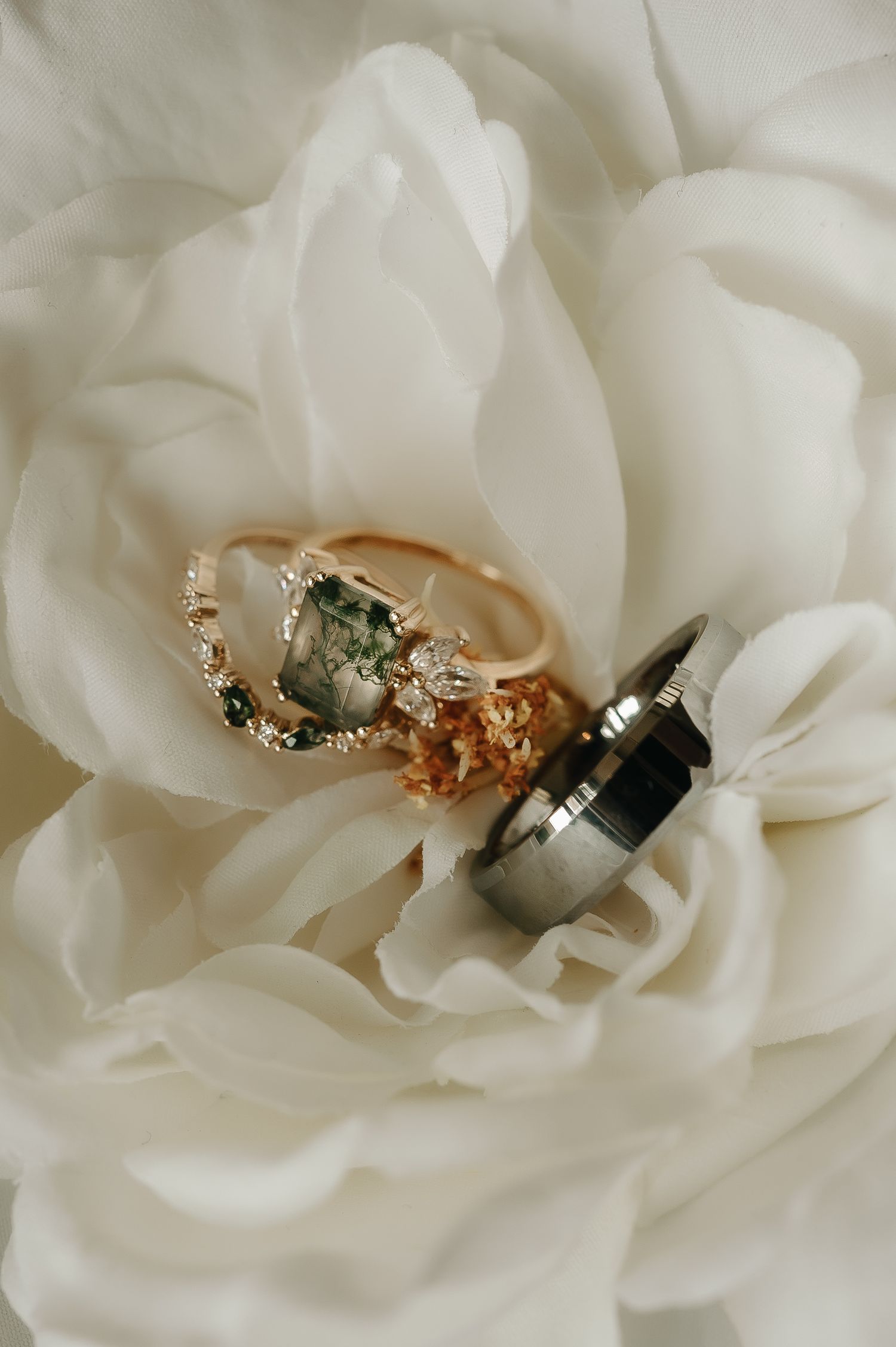 Wedding rings nestled in delicate white rose petals creating elegant jewelry detail shot.