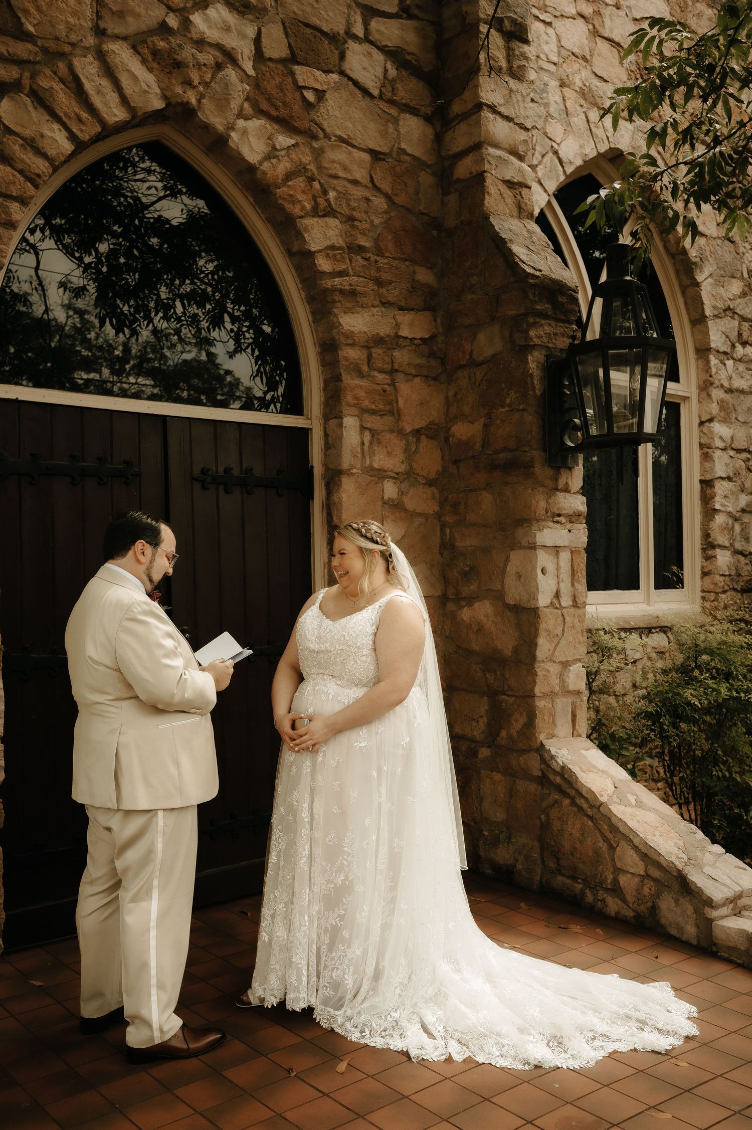 Wedding couple exchanging vows in front of a beautiful stone archway with rustic wooden doors.