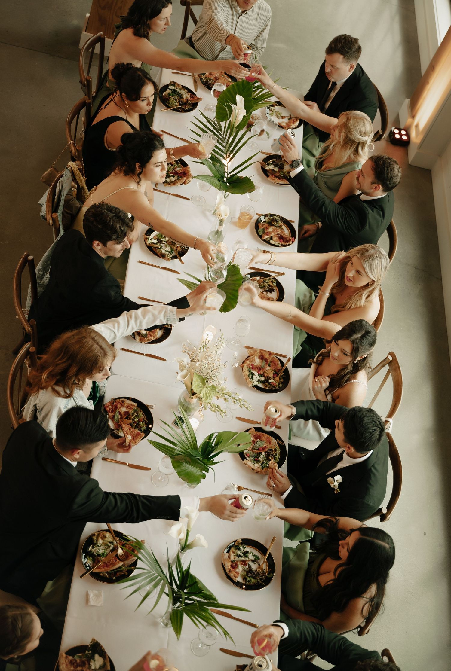 Aerial view of wedding guests seated at a long white table, sharing a meal with tropical floral centerpieces.