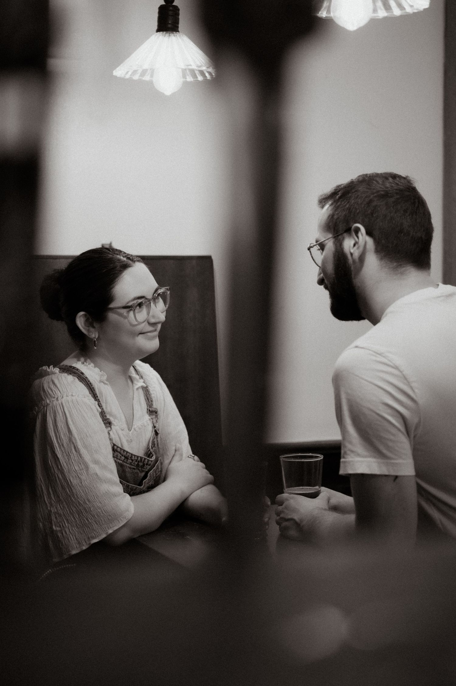 A man and woman sharing a conversation at a dimly lit pub booth, captured in black and white photography.