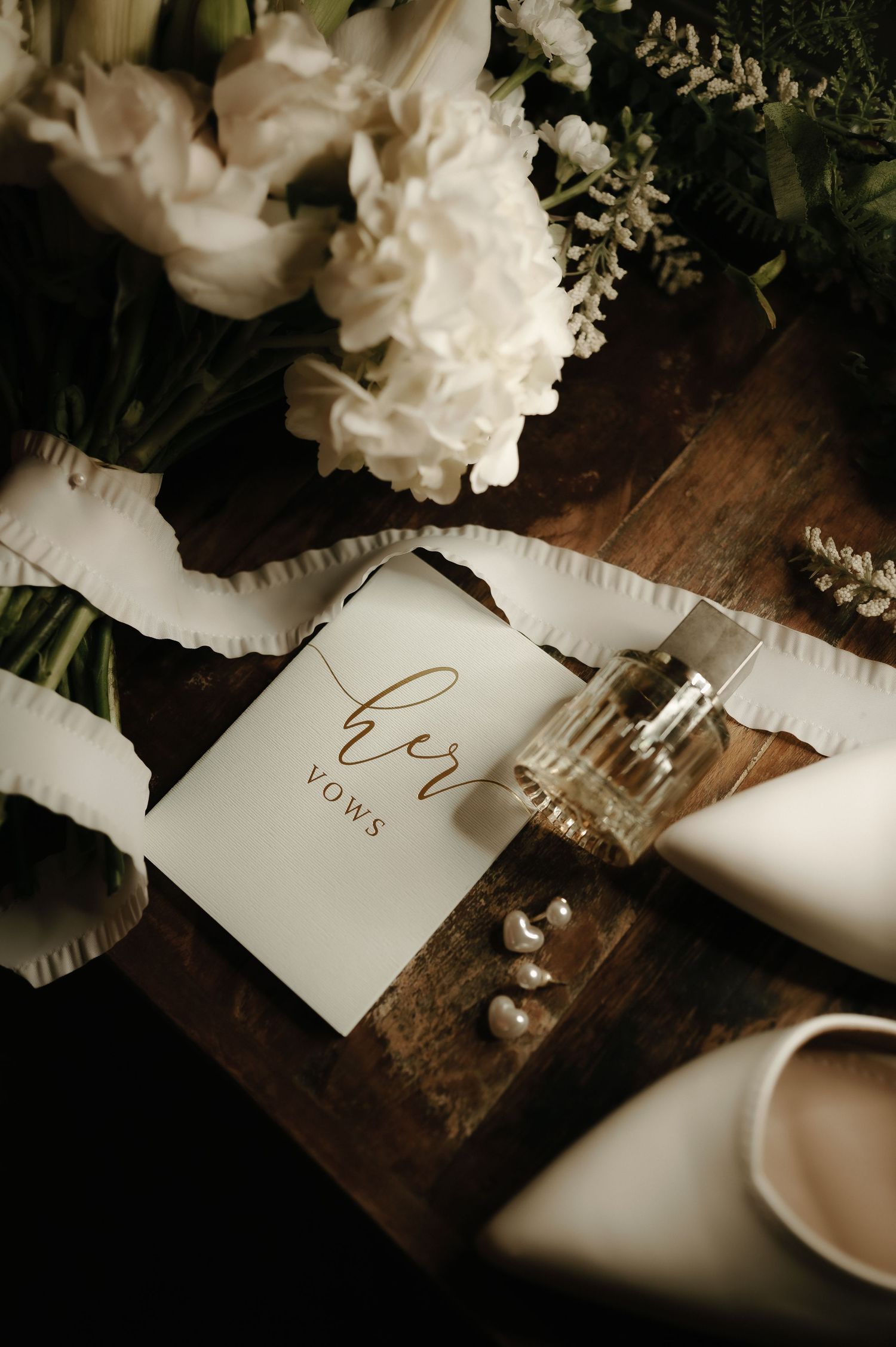 Elegant wedding details with white flowers and vows on rustic wooden surface.