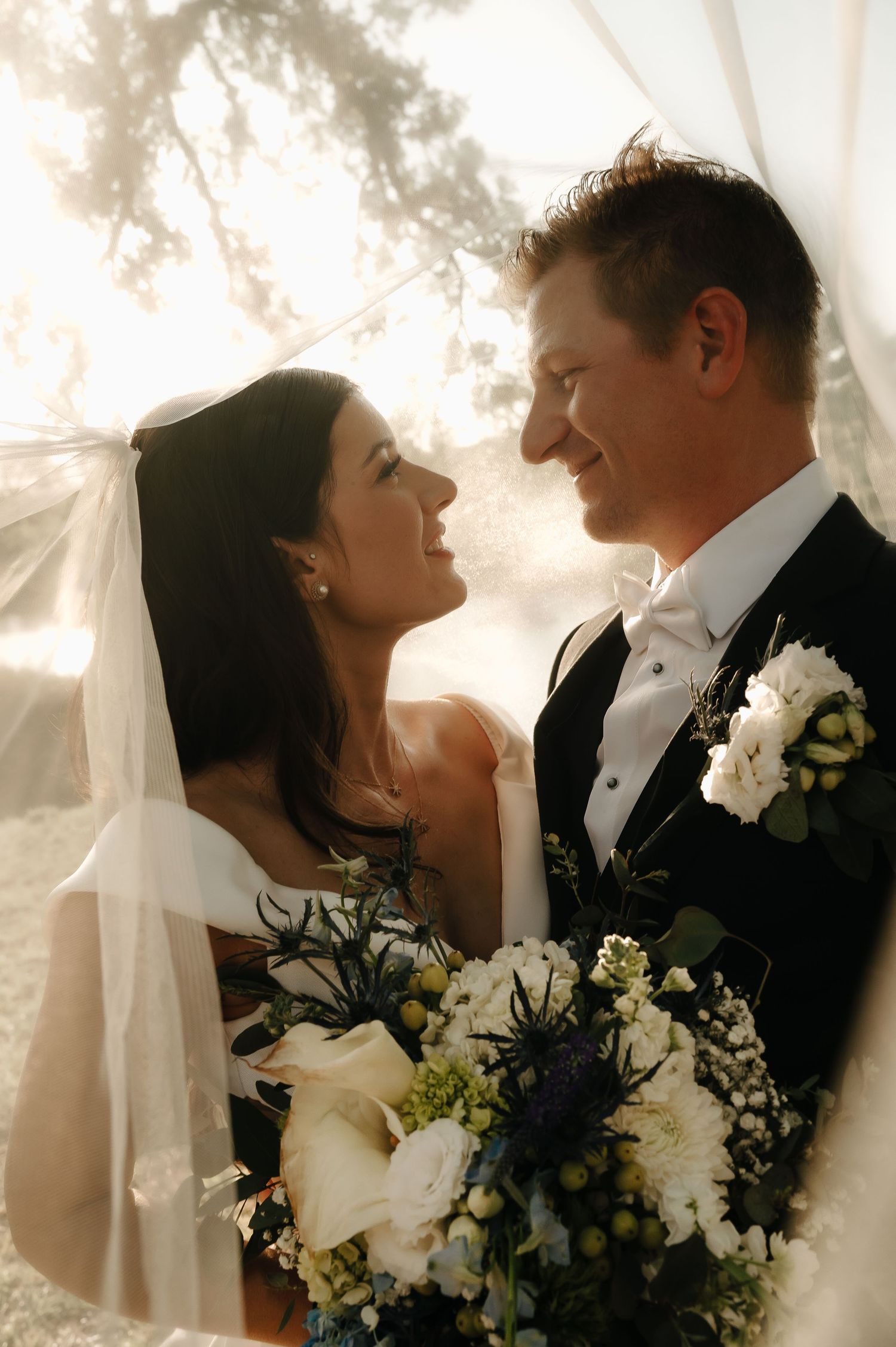 Romantic wedding couple embraces with white flowers and soft lighting creating an intimate moment.