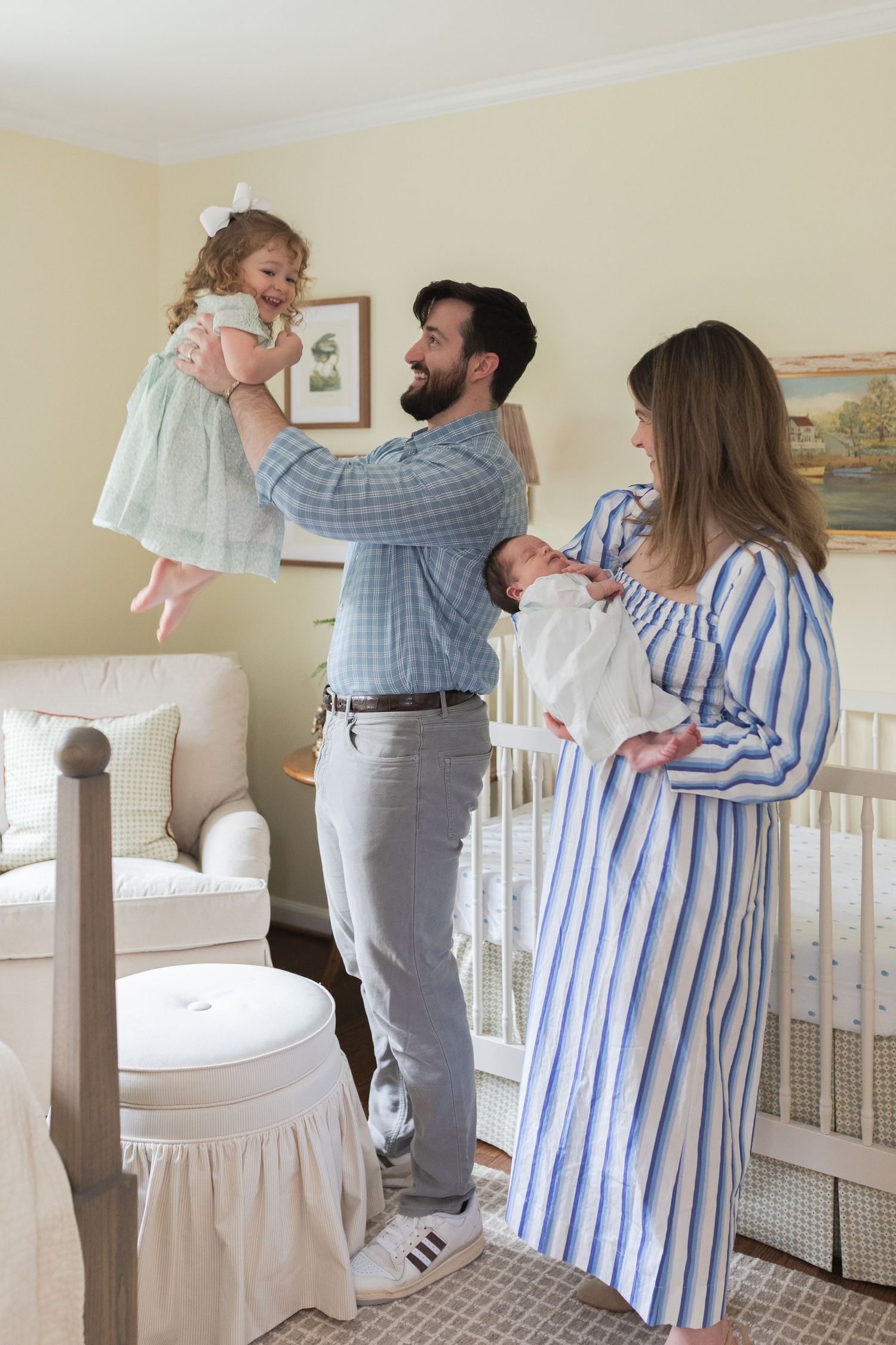 Sweet family interactions unfold in a nursery with white crib and soft natural lighting.