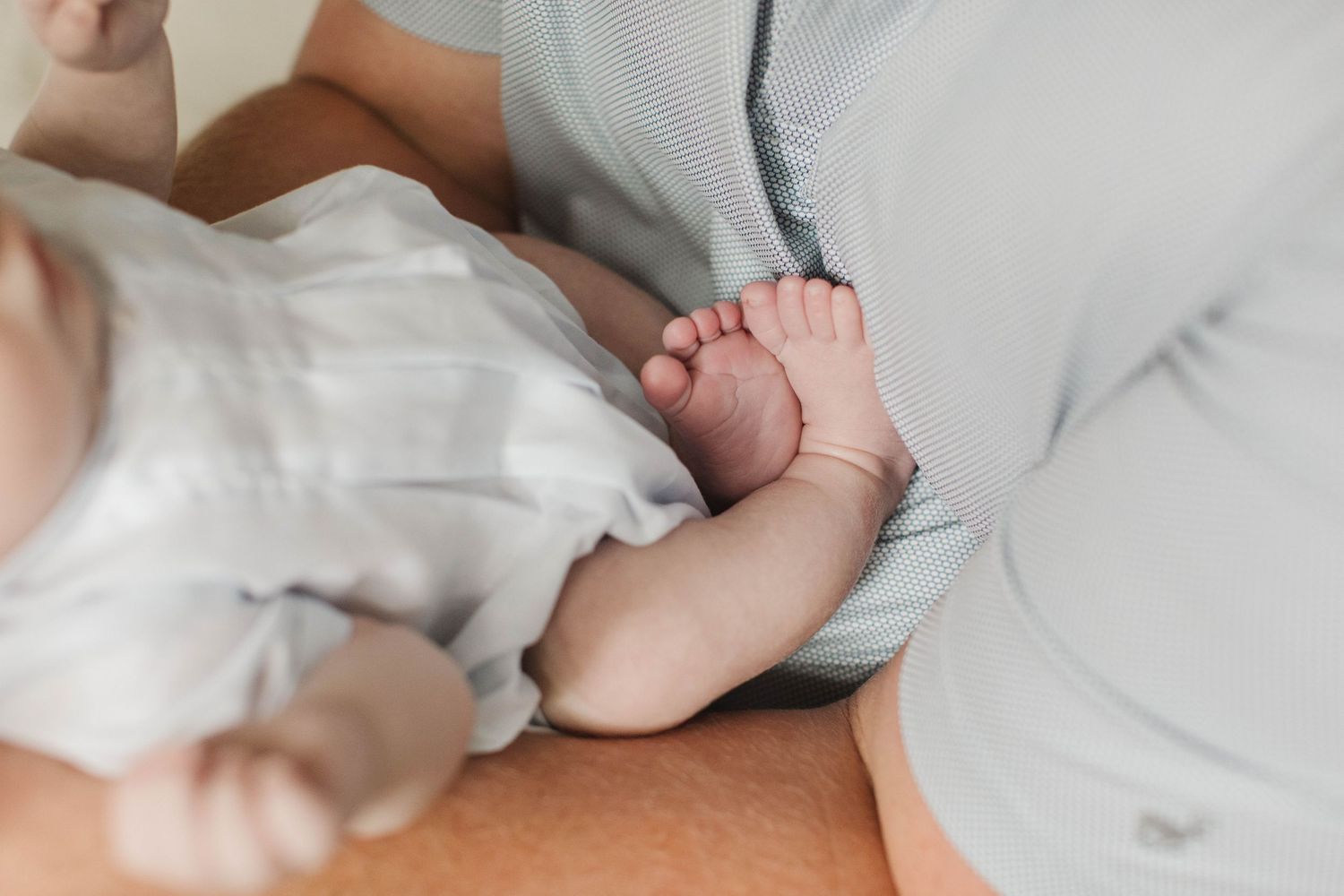 Lifestyle newborn photography showing tiny baby feet and hands against white sheets.